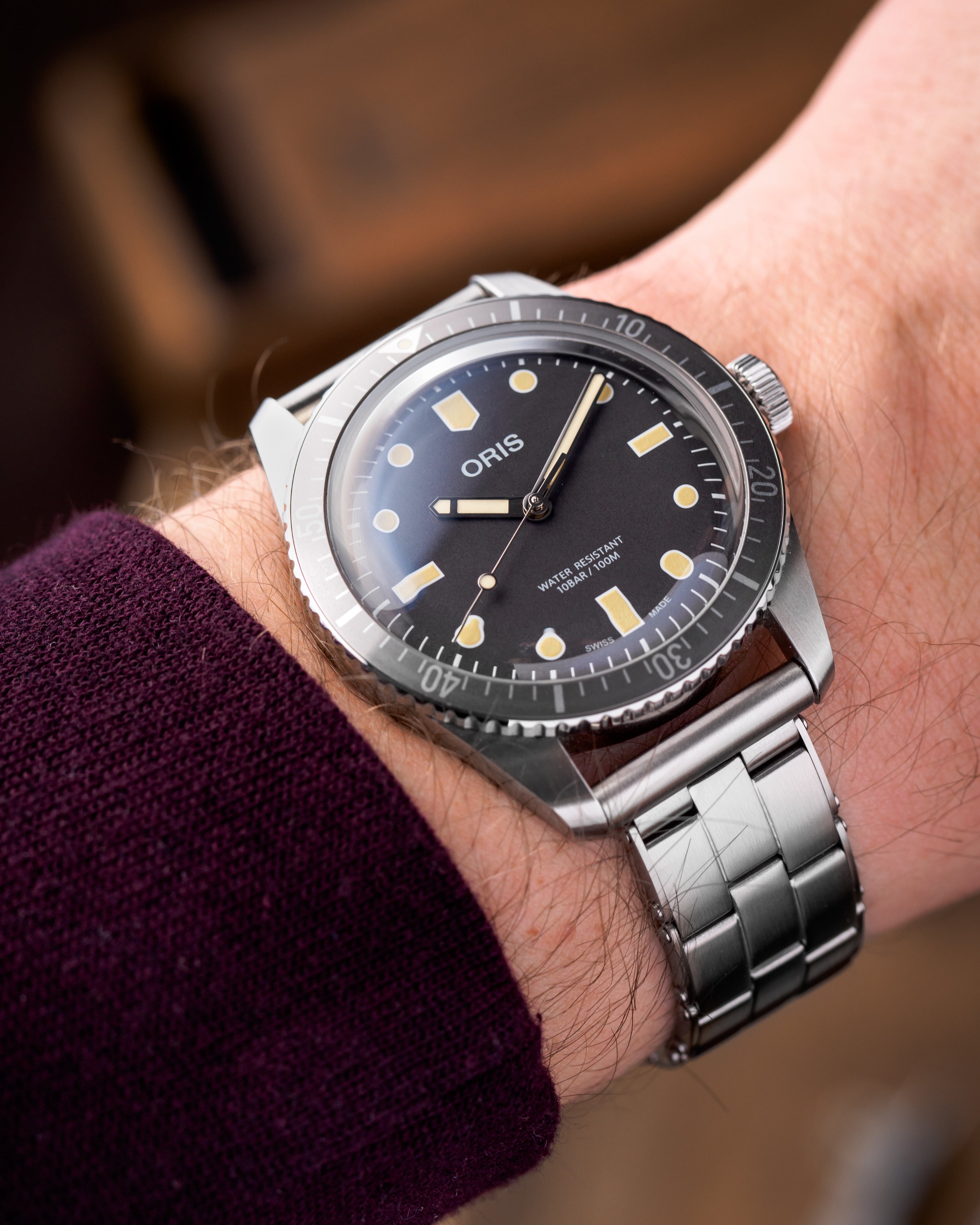 Oris diver watch with black dial, luminous indices, rotating bezel on stainless steel bracelet worn on wrist with purple sleeve
