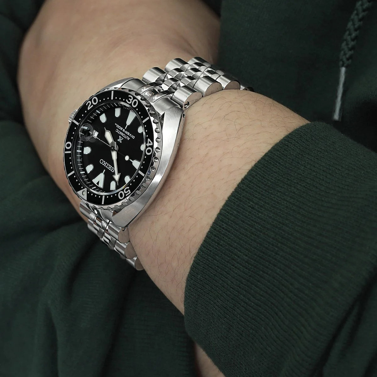 Silver stainless steel jubilee bracelet watch with black dial and rotating bezel worn on wrist