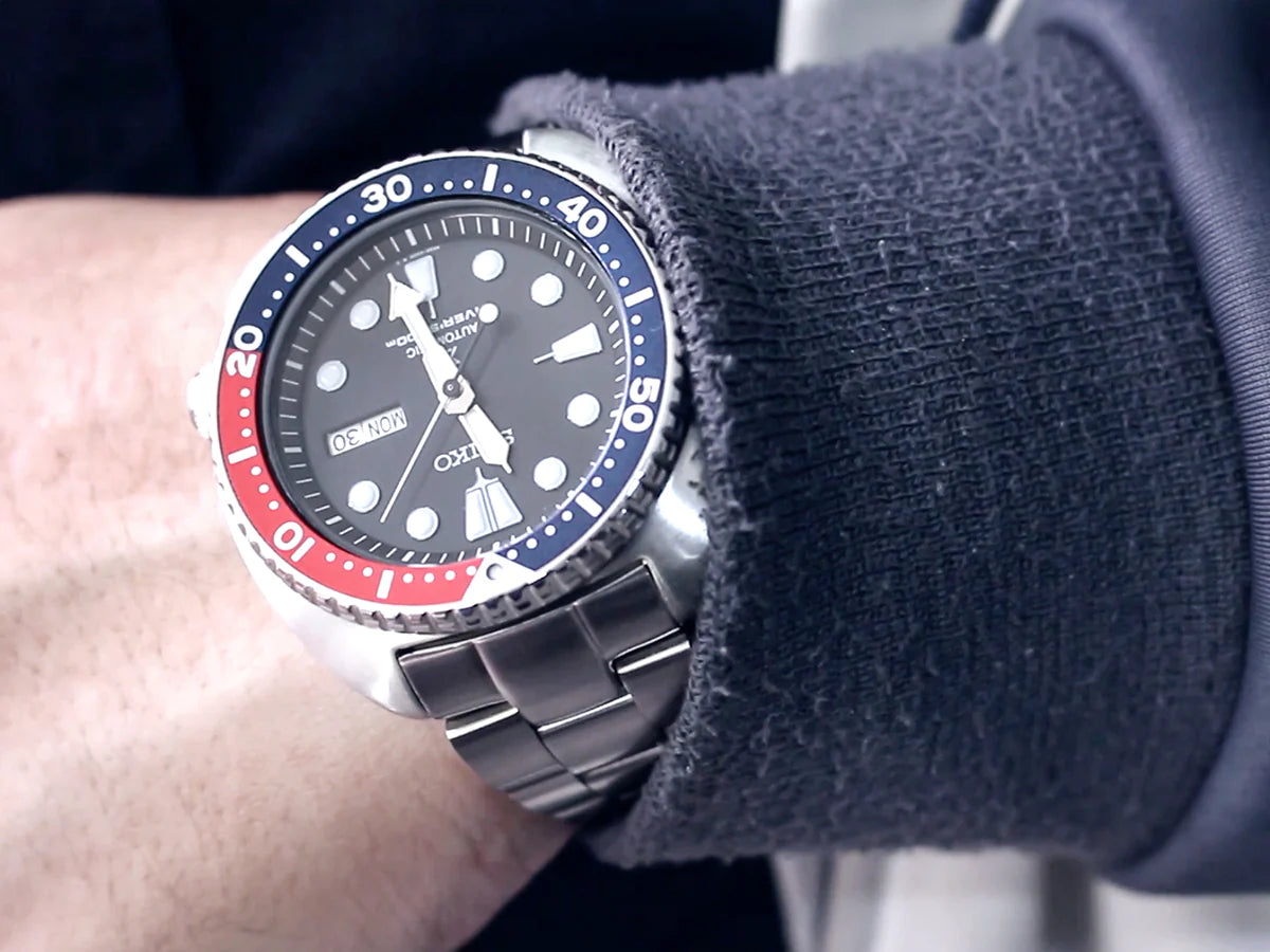 Seiko Turtle dive watch with red-blue bezel on stainless steel bracelet worn on wrist with gray sweater