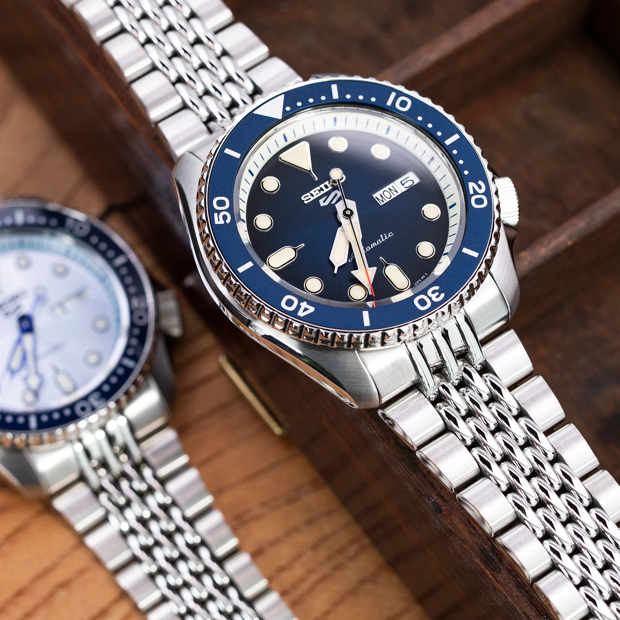 Seiko 5 dive watch with stainless steel jubilee bracelet and blue bezel on wooden surface