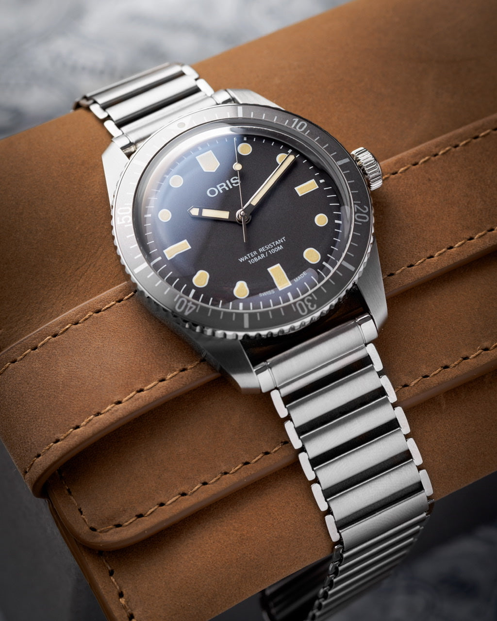 Oris dive watch with black dial and applied indices on stainless steel bracelet, displayed on tan leather strap