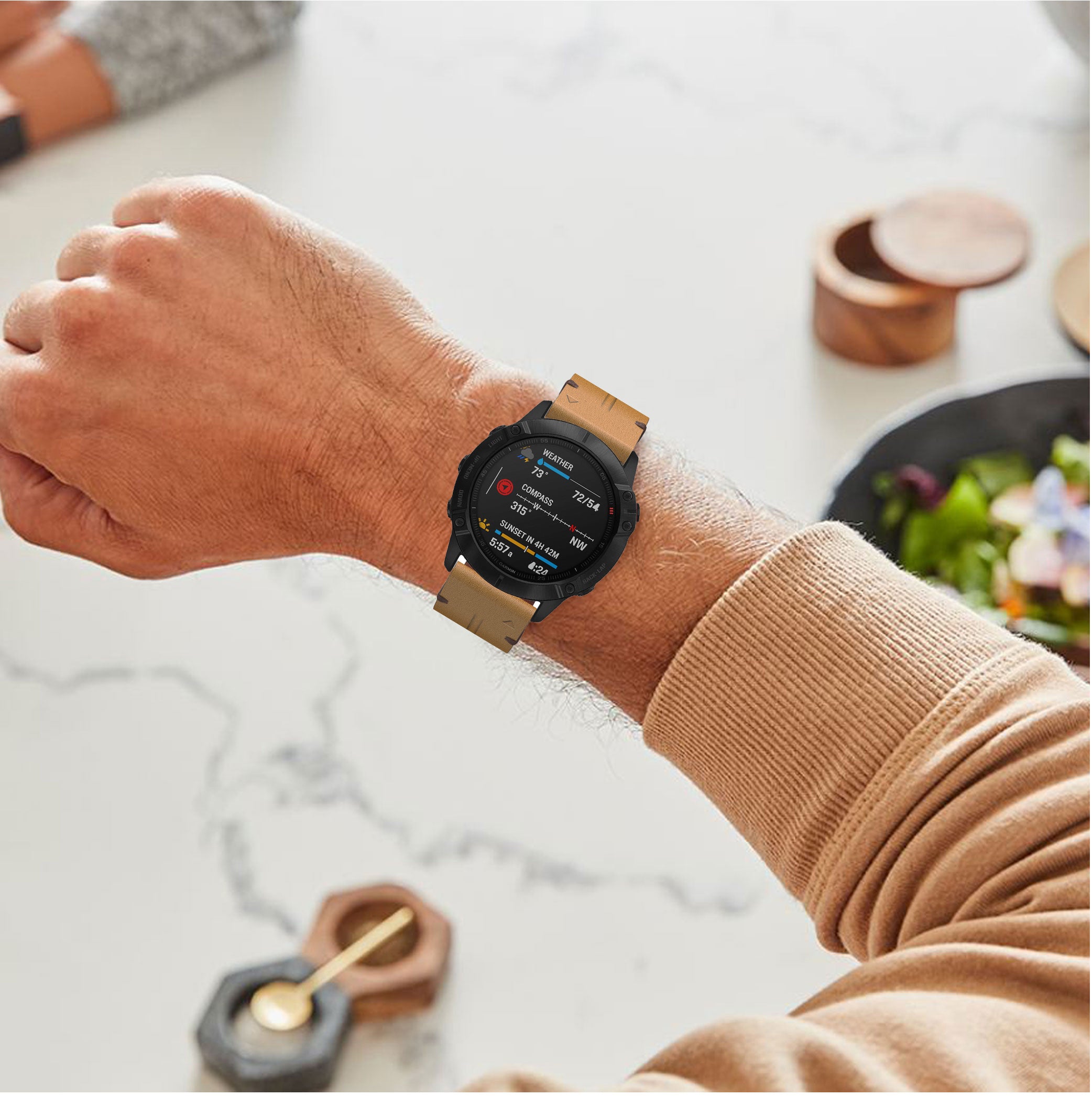 Man wearing black smartwatch with brown leather strap and tan sweater, displaying weather and fitness data on screen