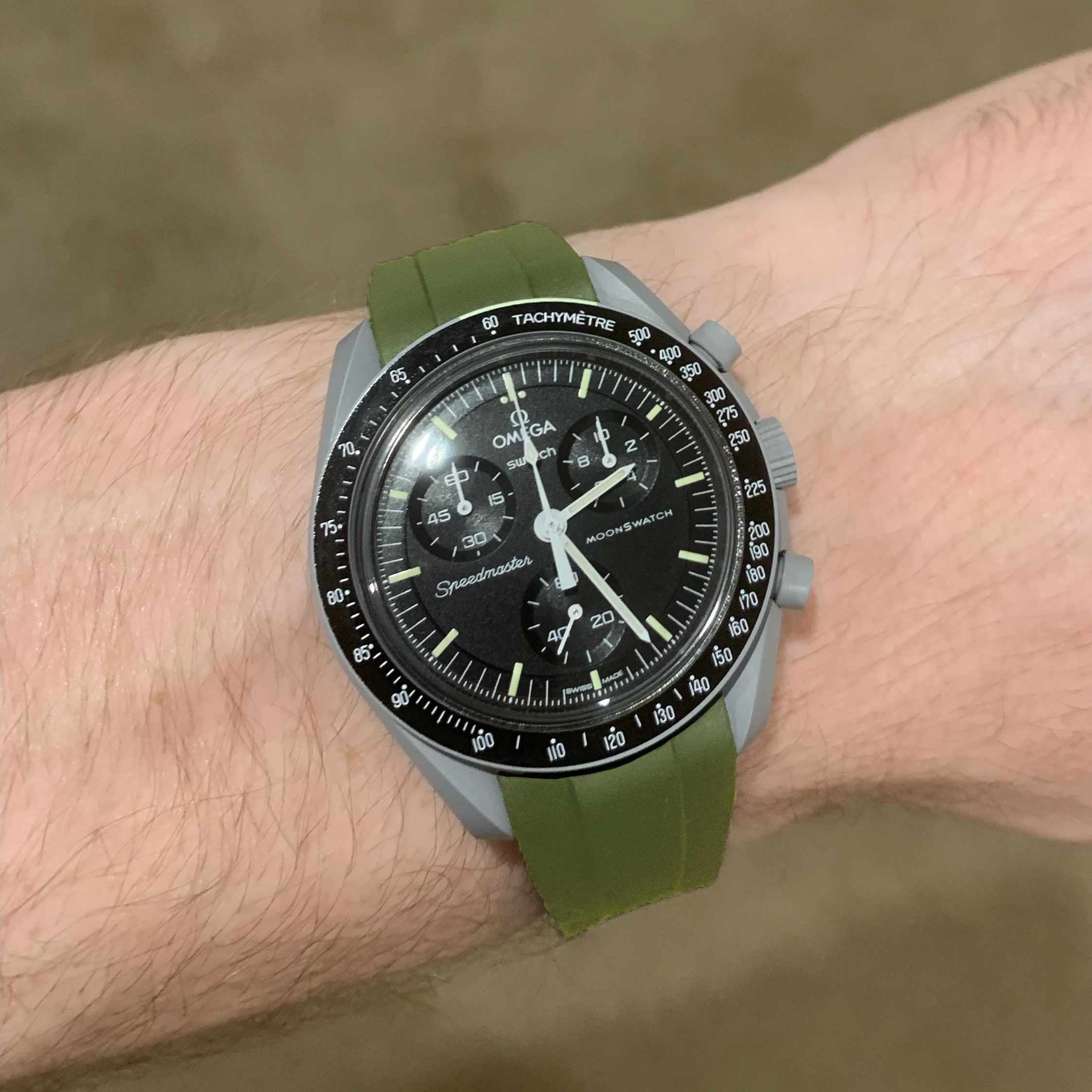 Omega MoonSwatch Speedmaster chronograph watch with black dial, tachymeter bezel, and green rubber strap on wrist