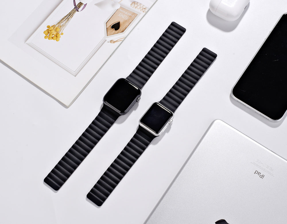 Two black magnetic silicone loop bands for smartwatch displayed on white background with tech accessories