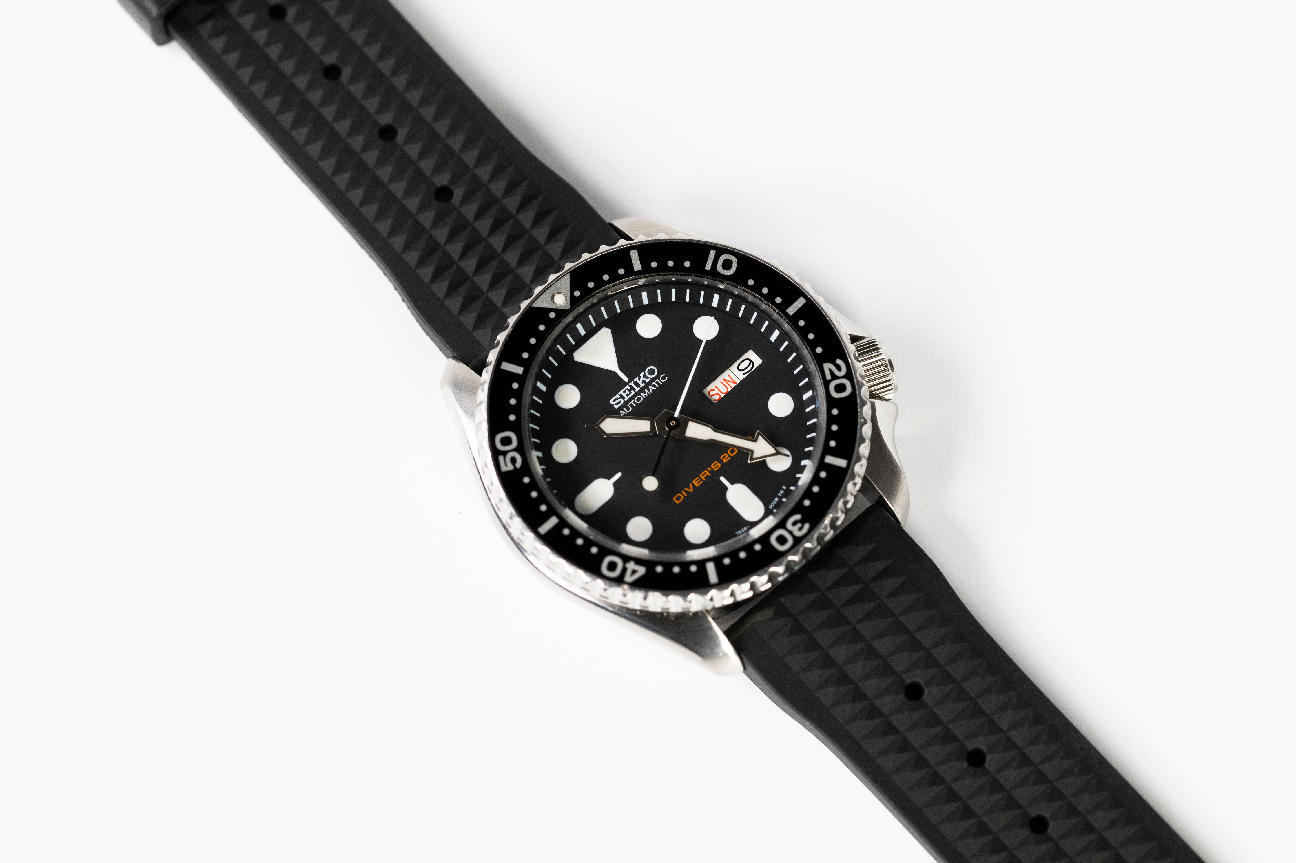 Seiko SKX diving watch with black dial, white hour markers, and black rubber strap with quick release deployment clasp