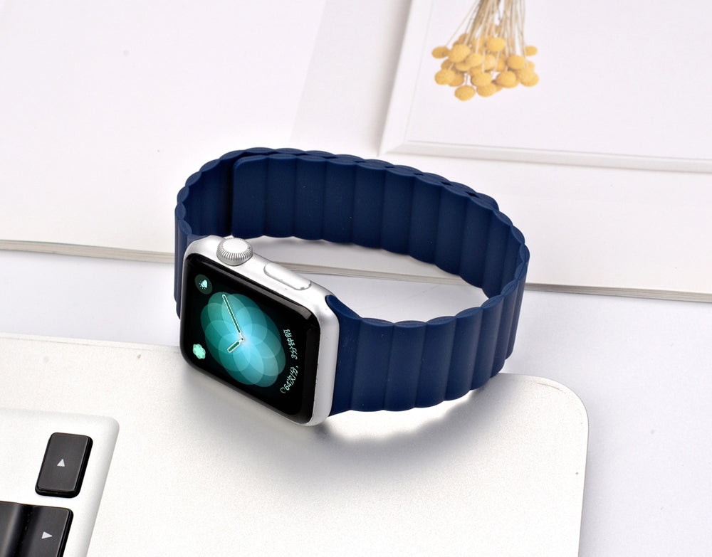 Smartwatch with silver case and navy blue magnetic silicone loop band displaying turquoise watch face on white desk