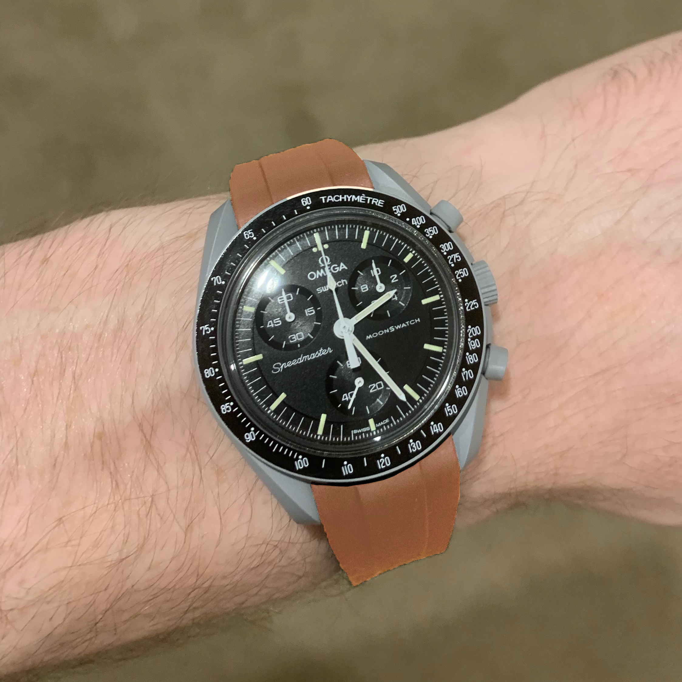 Omega Swatch MoonSwatch Speedmaster chronograph watch with black dial, brown rubber strap, and tachymeter bezel on wrist