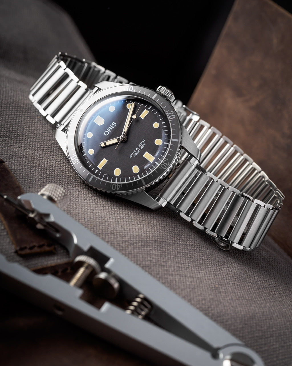 Oris dive watch with black dial and gold markers on stainless steel bracelet displayed on gray fabric