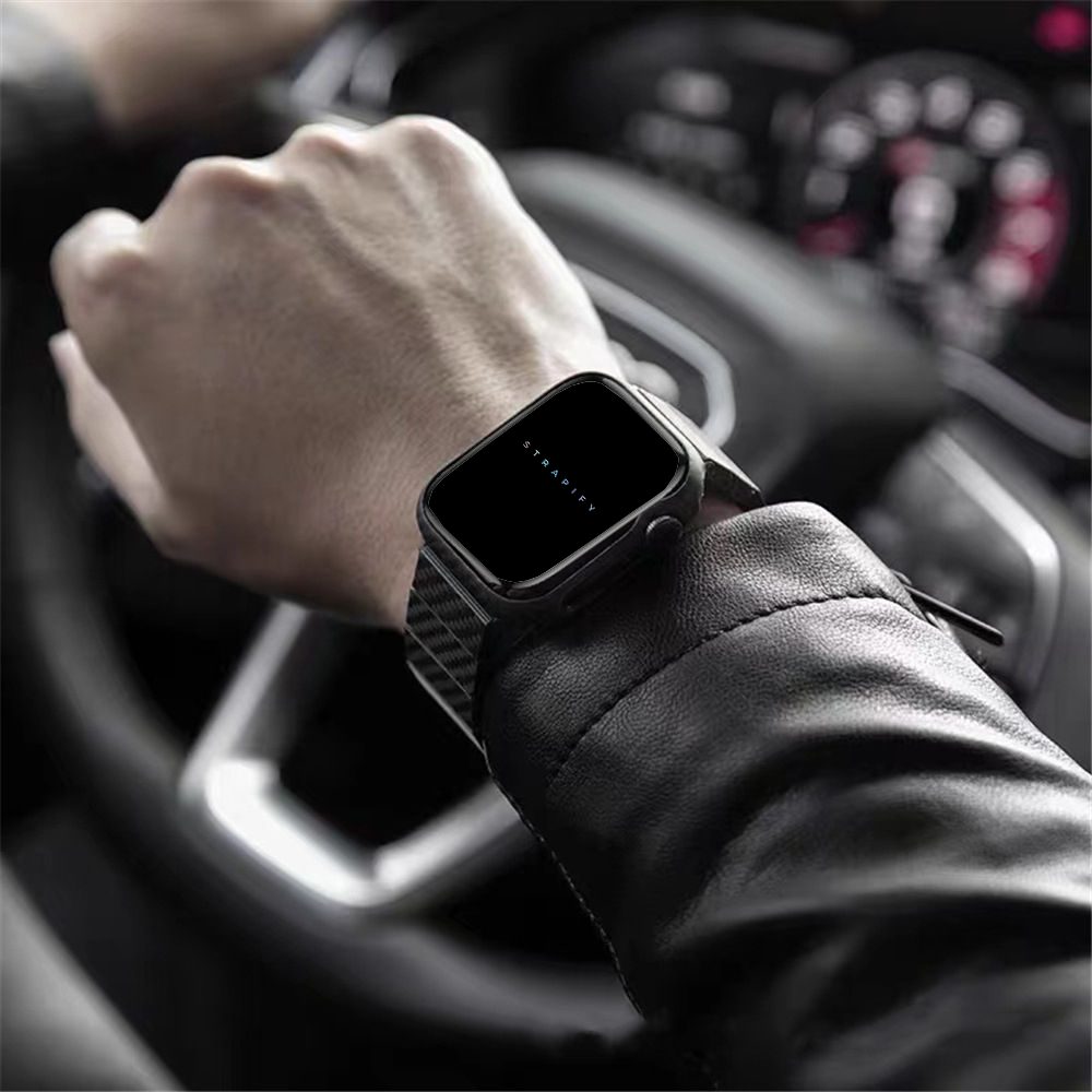 Black carbon fiber smartwatch bracelet on wrist inside car with steering wheel visible