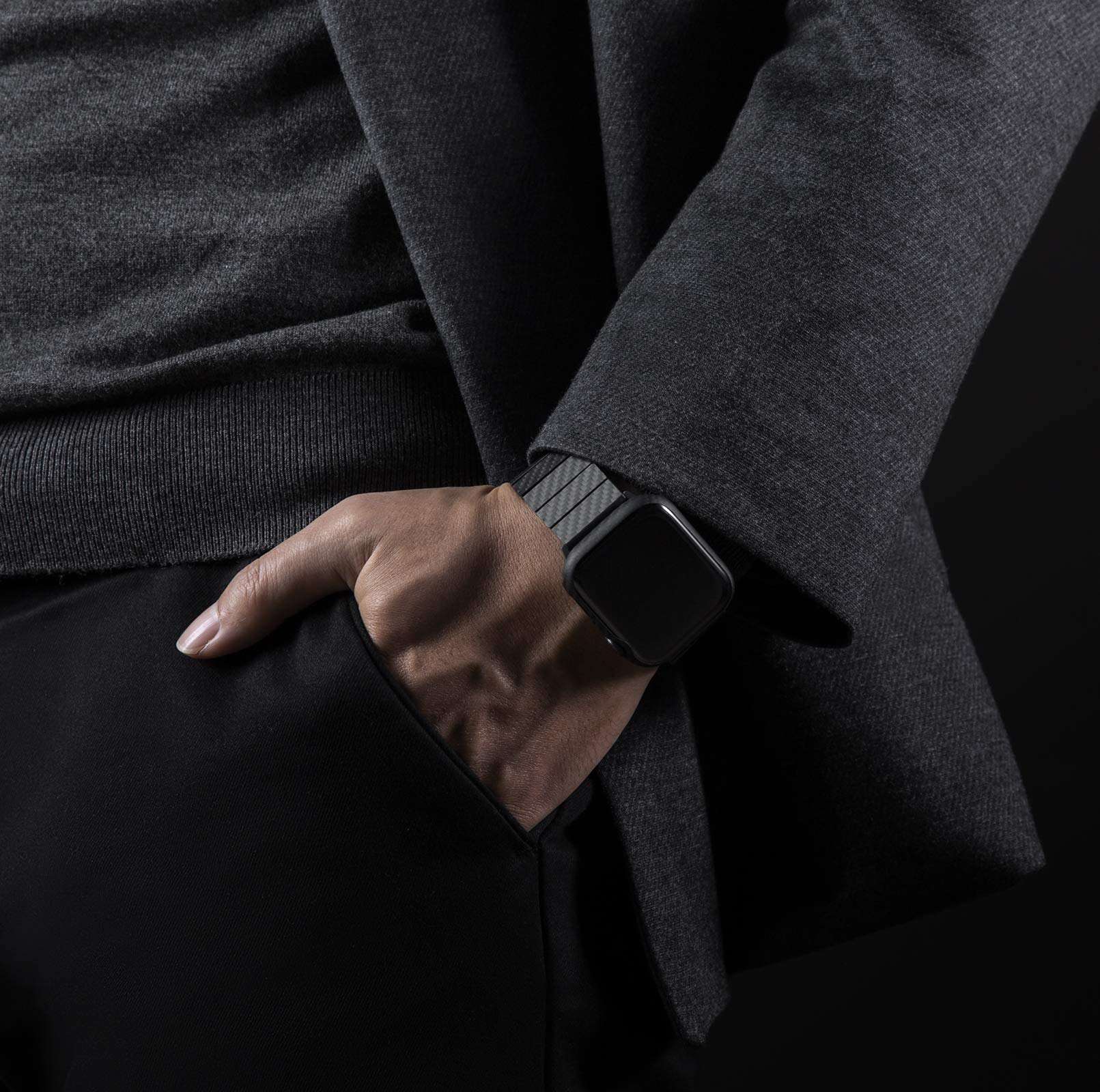 Black carbon fiber smartwatch band on man's wrist wearing dark grey blazer and black shirt, close-up lifestyle shot