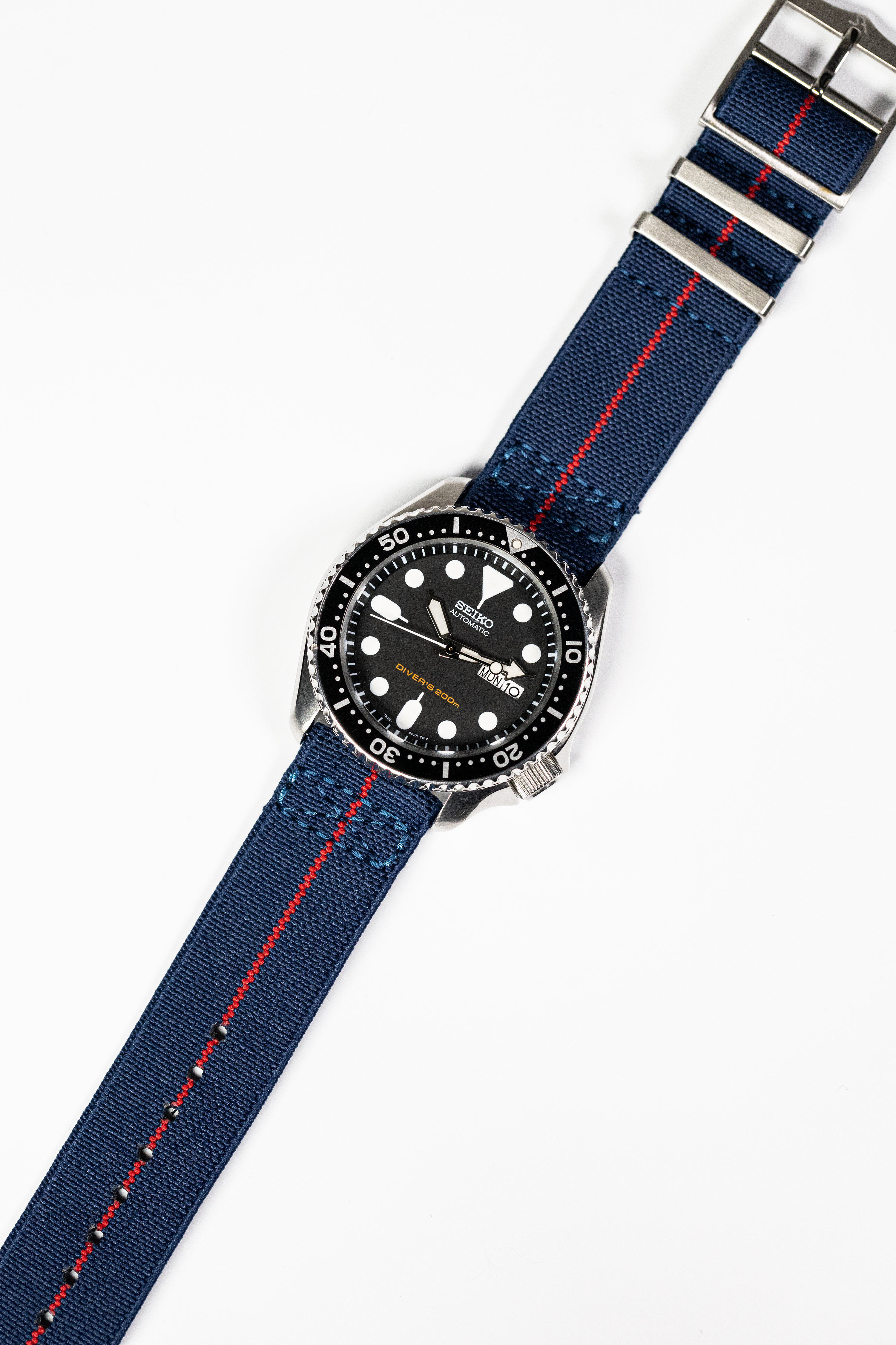 Seiko automatic dive watch with black dial, stainless steel case, and navy blue fabric strap with red stripe and quick release buckle