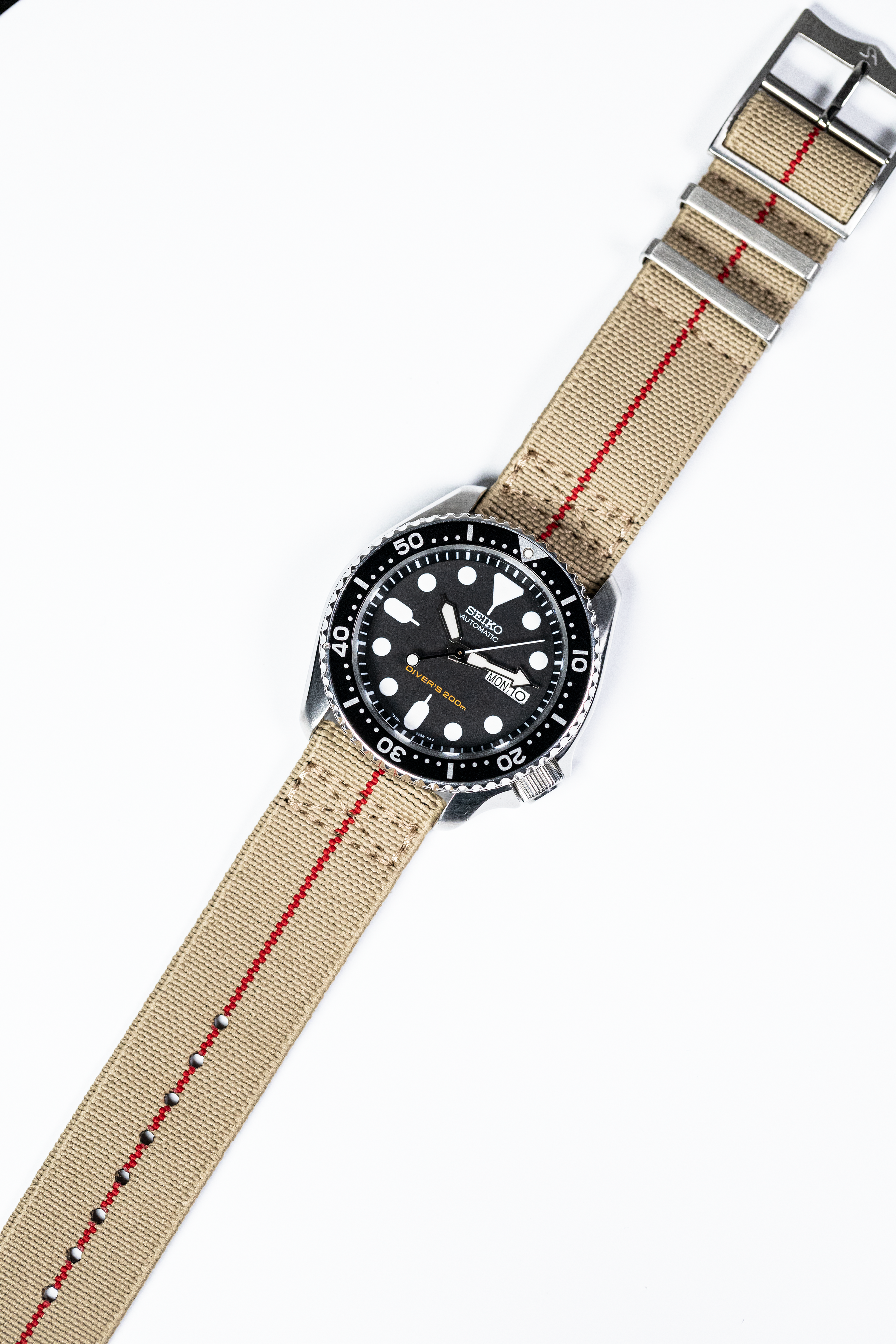 Seiko dive watch with black dial and stainless steel case on desert sand fabric strap with red stripe and quick release buckle