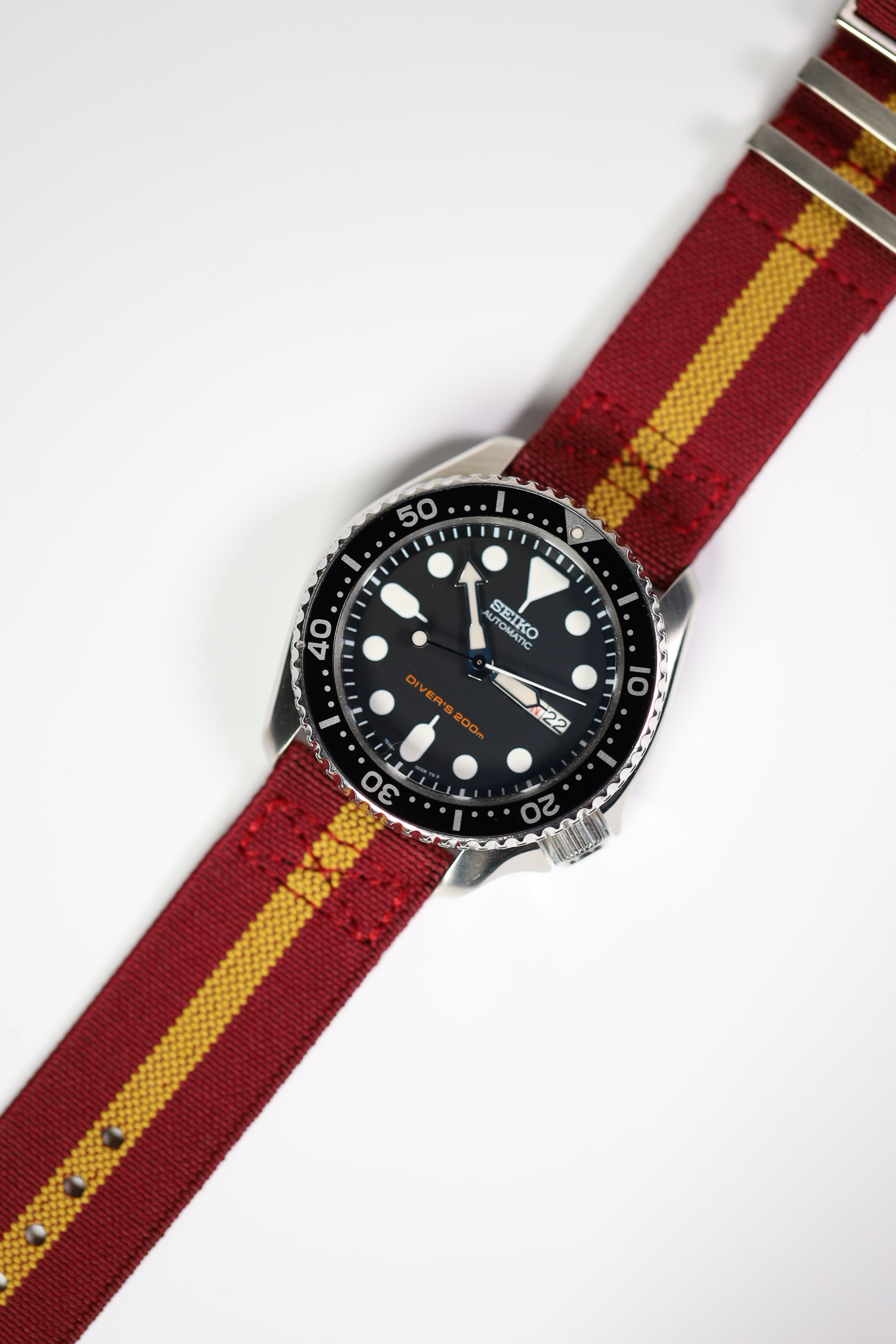 Seiko automatic dive watch with black dial and steel case on burgundy red and yellow striped fabric quick release strap