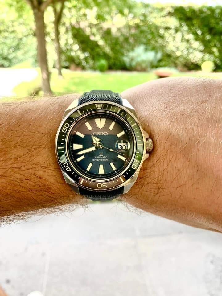 Seiko automatic dive watch with black dial and bezel on black hybrid rubber strap, worn on wrist outdoors
