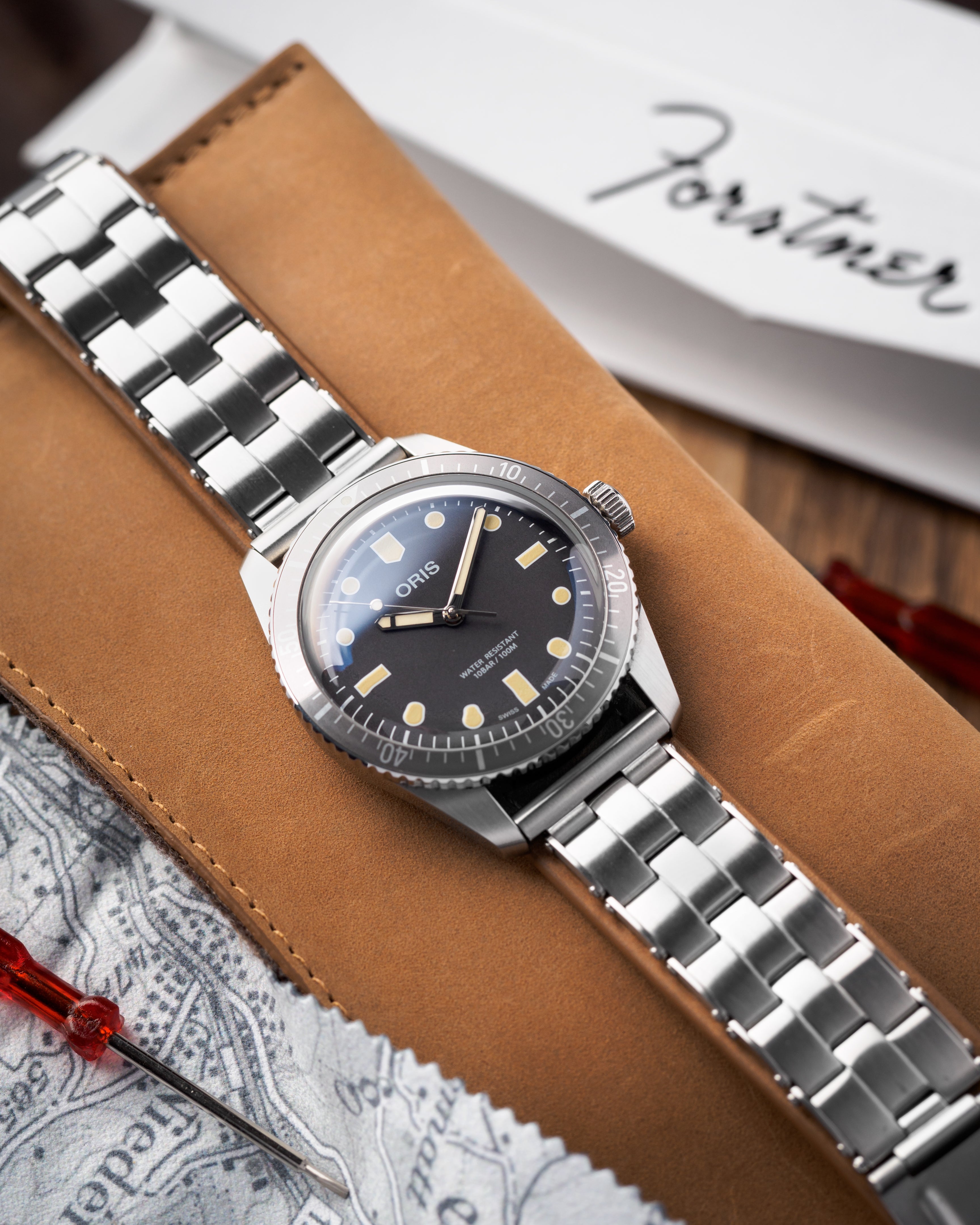 Oris vintage dive watch with black dial and gilt markers on stainless steel bracelet displayed on tan leather portfolio