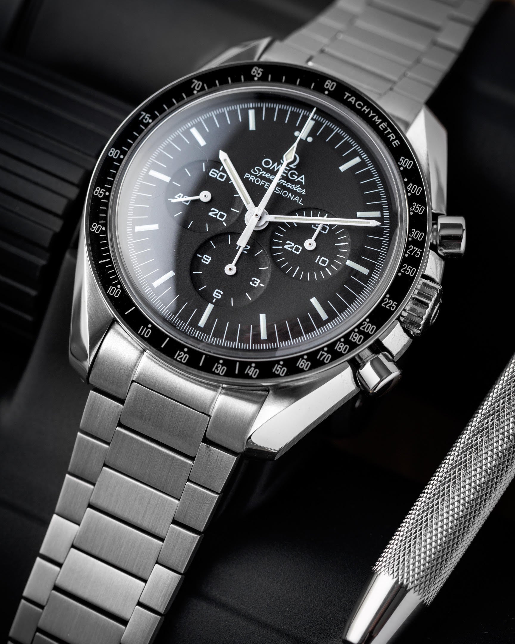 Omega Speedmaster Professional chronograph watch with black dial, tachymeter bezel, stainless steel bracelet on dark surface