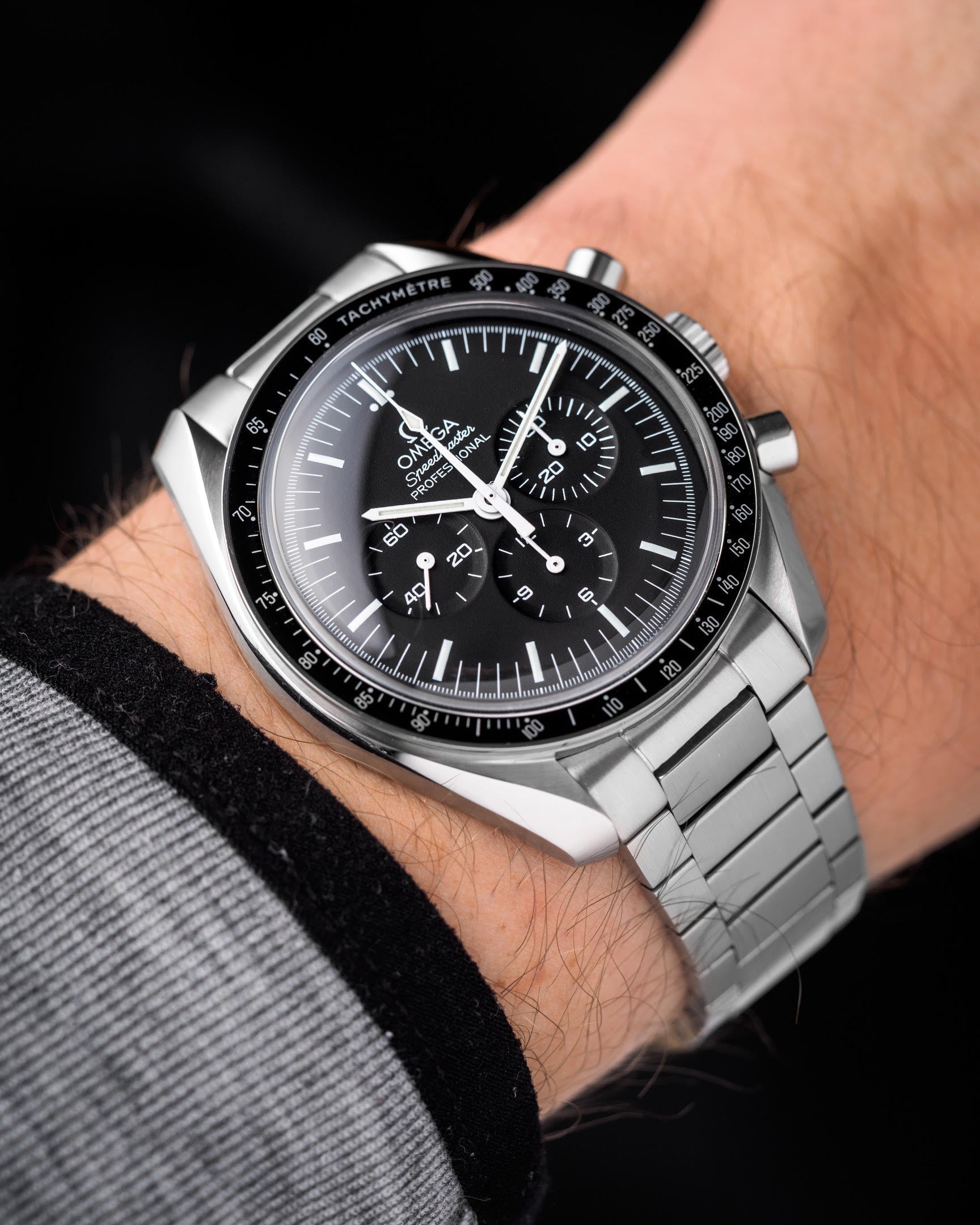 Omega Speedmaster chronograph watch with black dial and stainless steel Forstner flat link bracelet on wrist