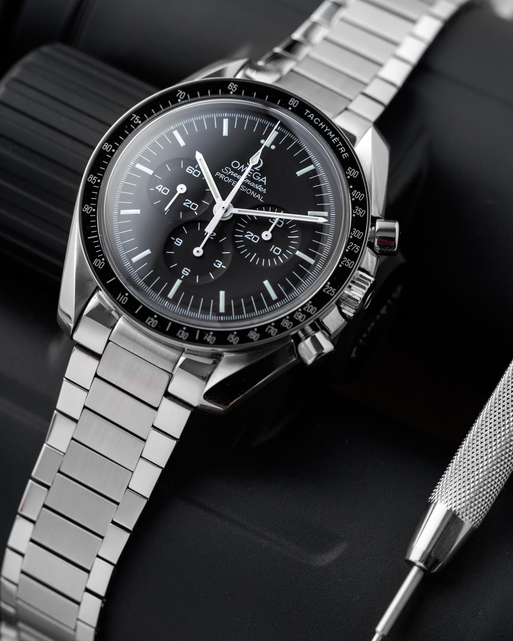 Omega Speedmaster Professional chronograph watch with black dial, steel bracelet, and tachymeter bezel on dark background