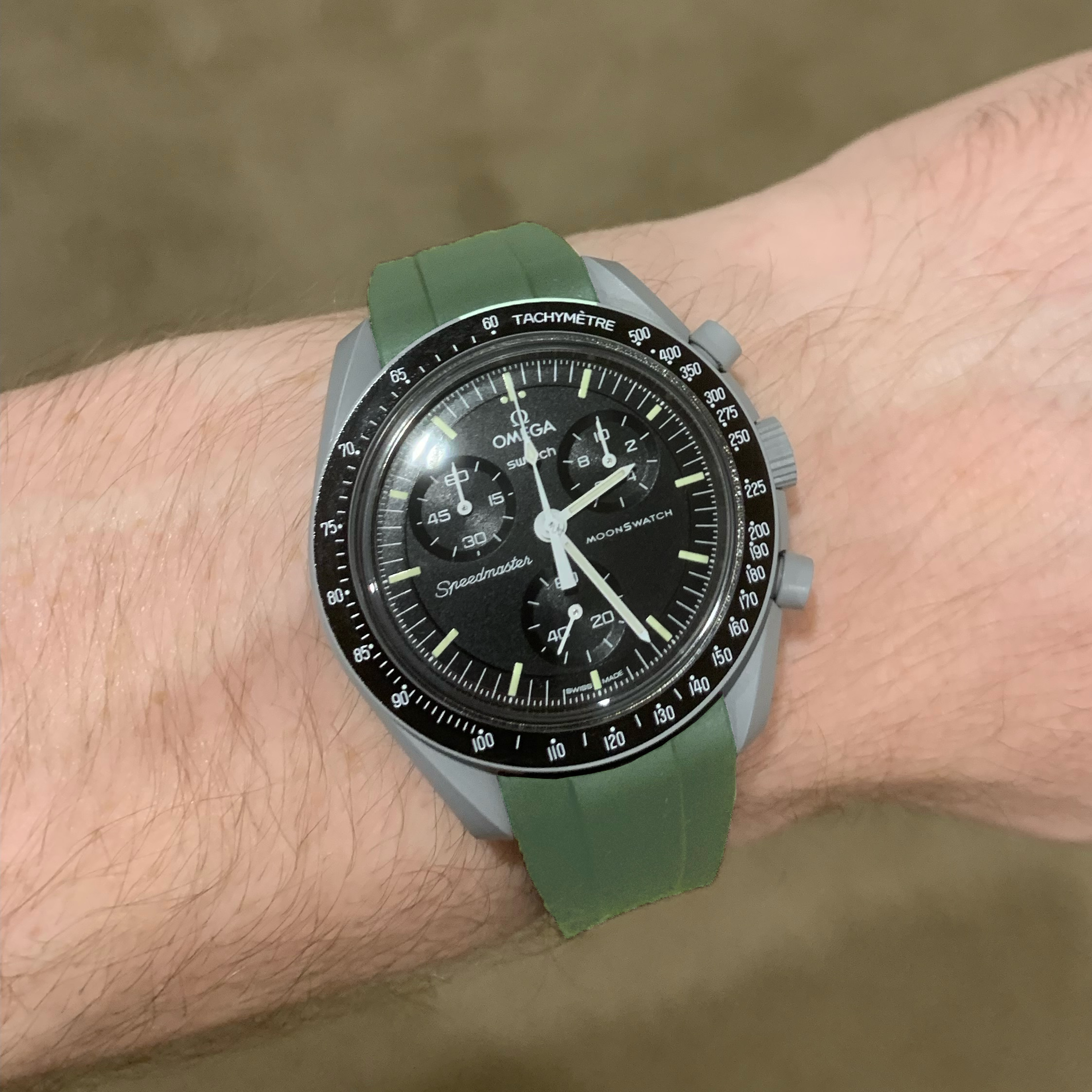 Omega MoonSwatch Speedmaster chronograph watch with black dial, tachymeter bezel, and forest green rubber strap on wrist