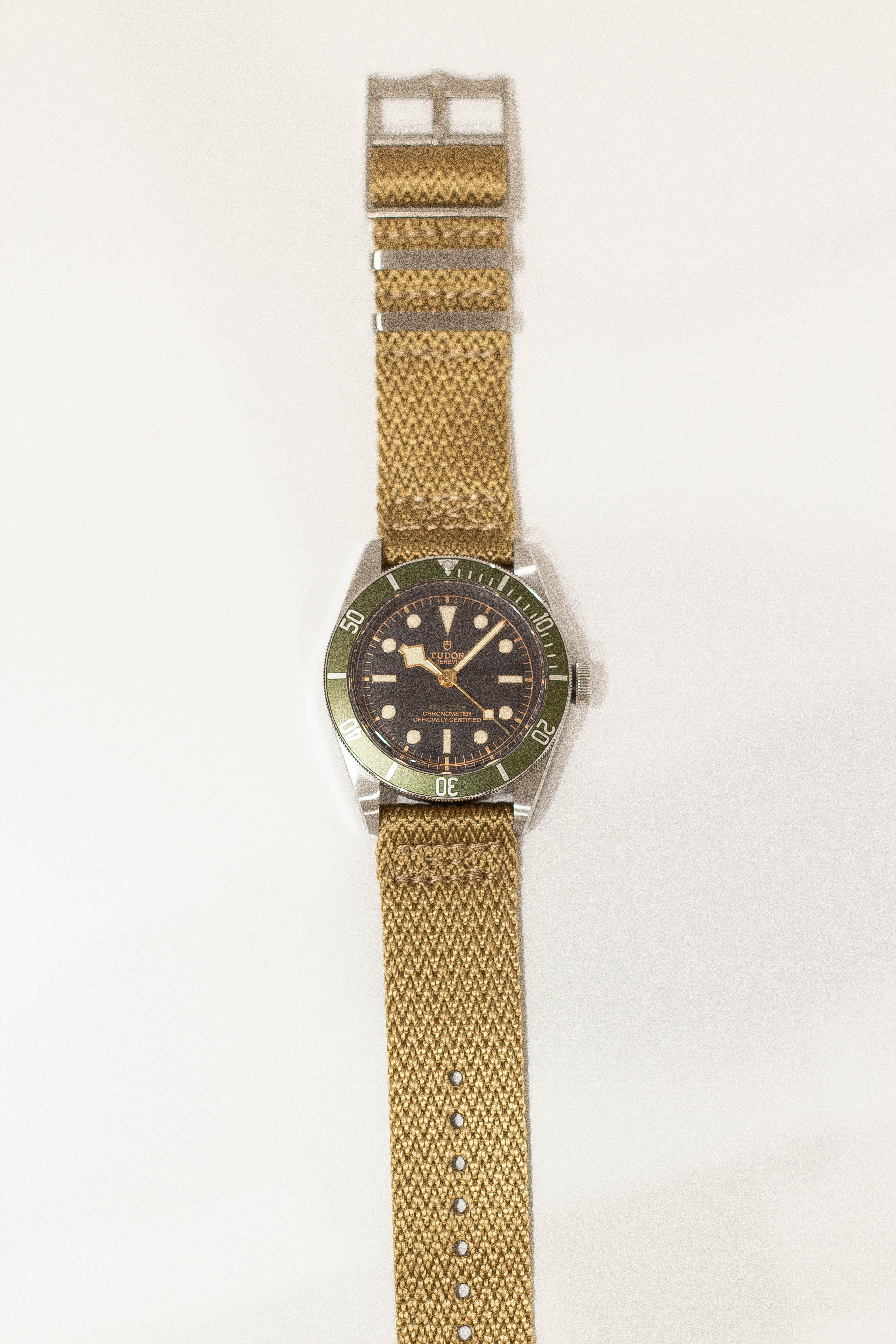 Tudor dive watch with green bezel, black dial, stainless steel case on khaki Militex fabric quick release strap