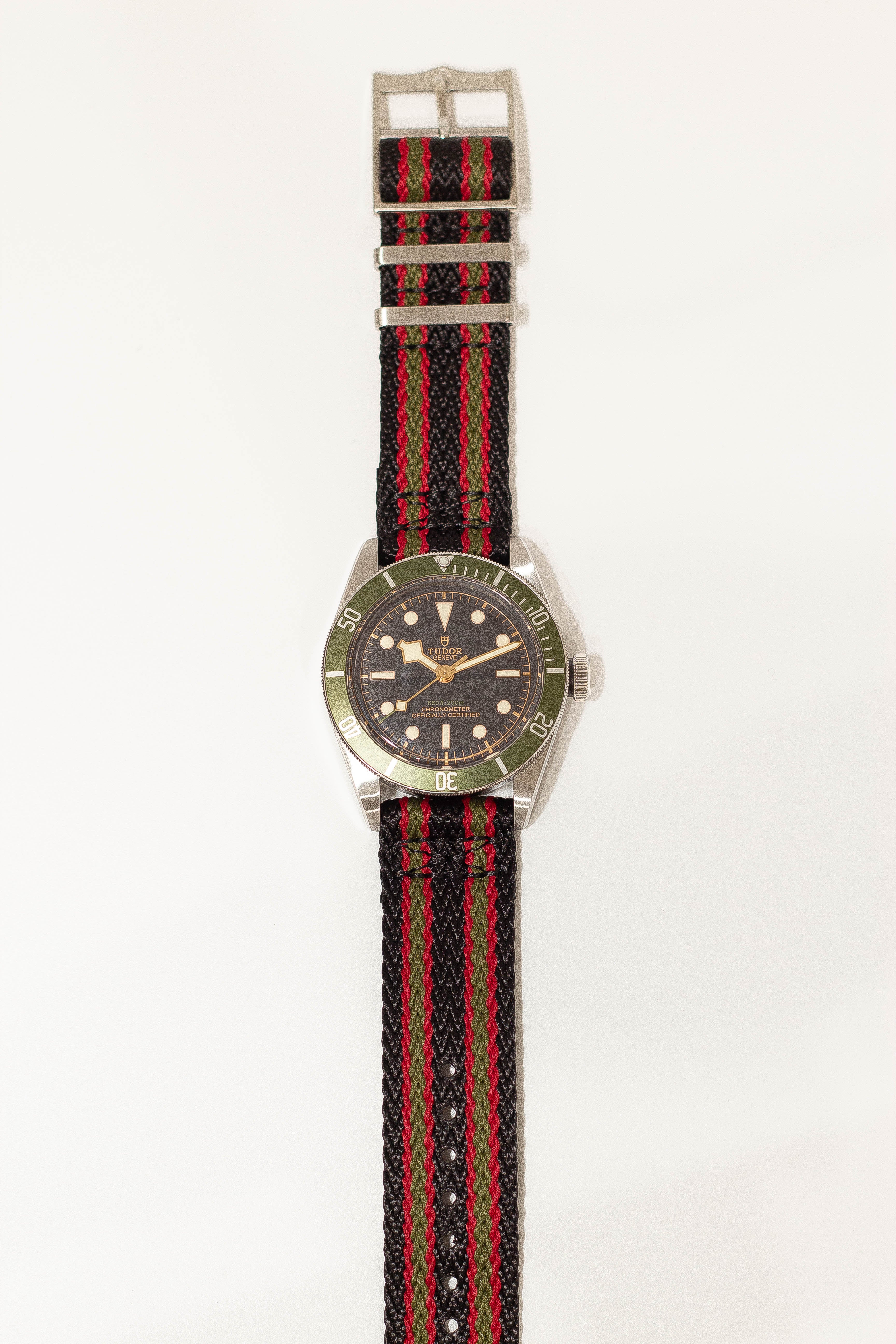 Tudor Black Bay dive watch with green bezel and military striped fabric strap in black, red, and green