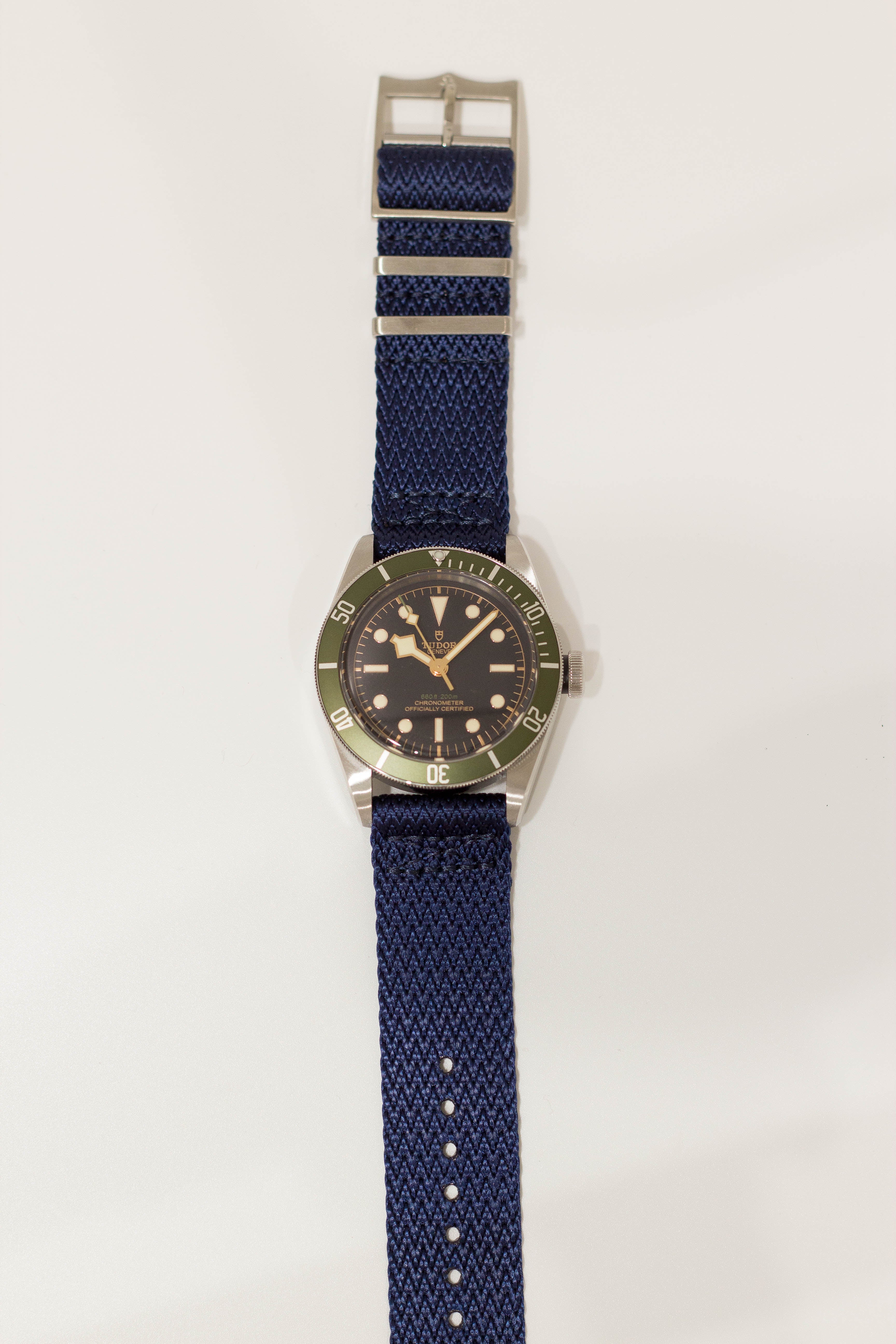 Men's dive watch with green bezel, black dial, and navy blue fabric quick release strap with metal buckle