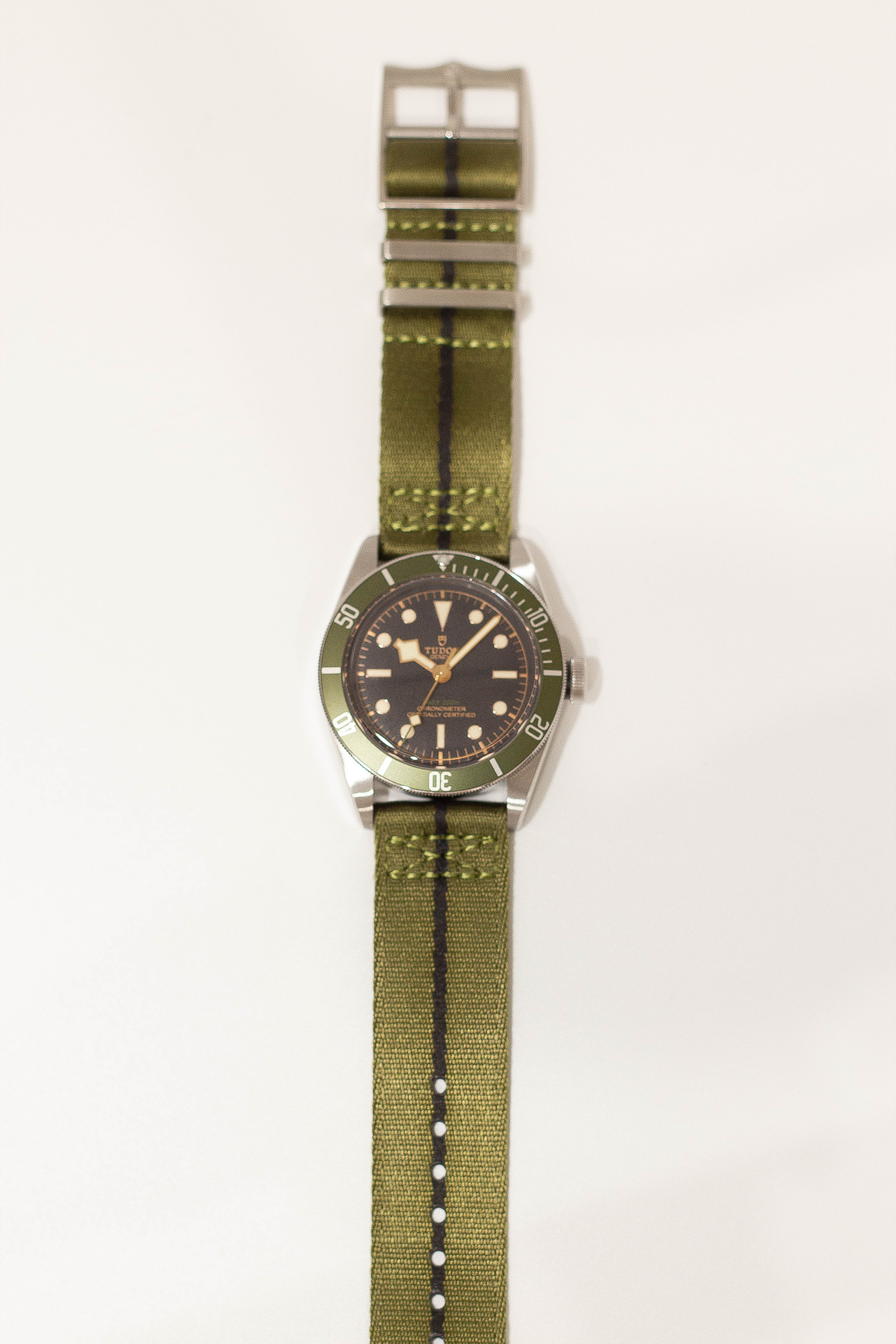 Vintage dive watch with black dial and green bezel on olive green fabric strap with quick release buckle