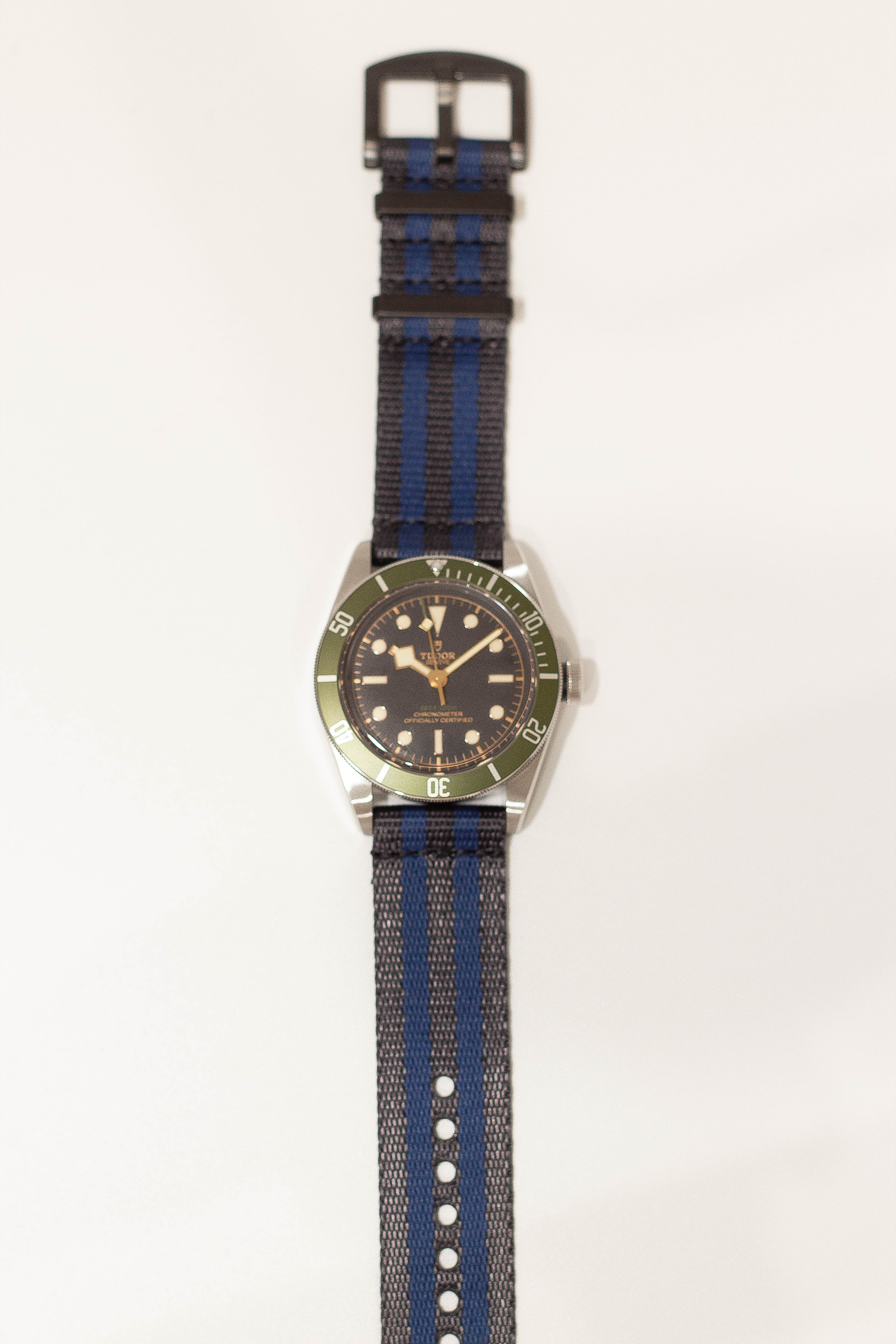Tudor dive watch with green bezel, black dial, and dark blue striped fabric strap with quick release buckle
