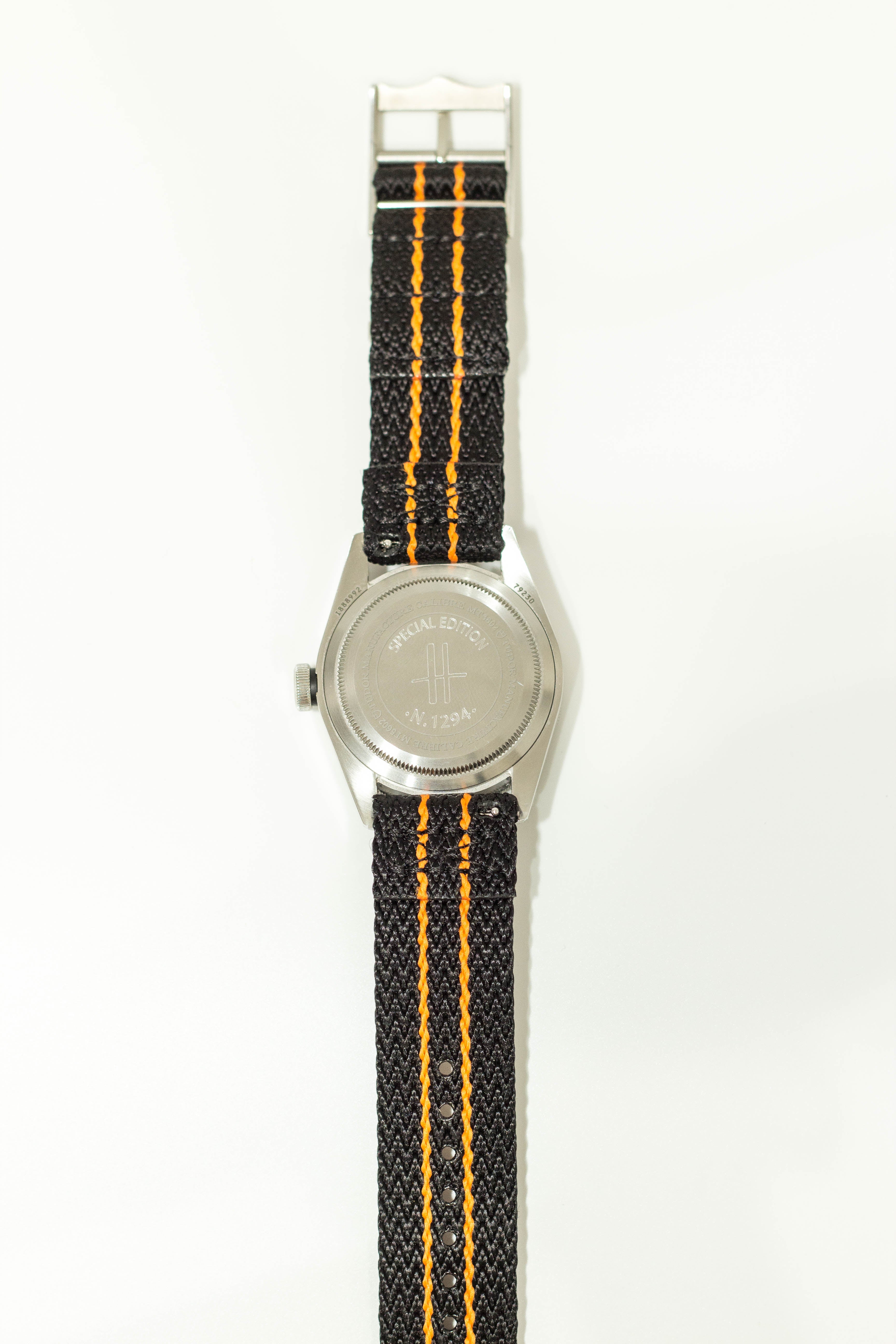 Stainless steel military watch with black canvas strap featuring orange double stripe detail and quick release buckle