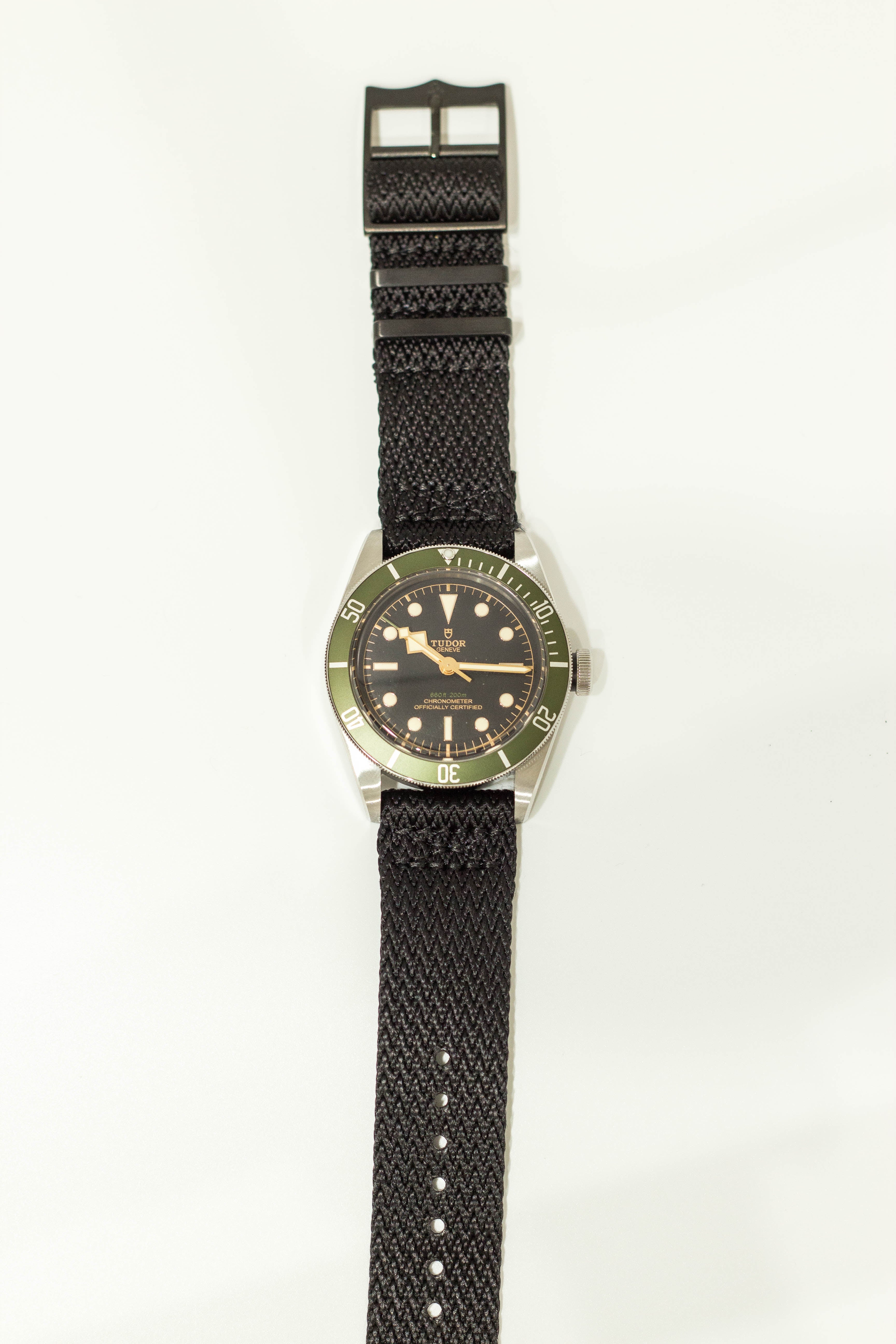 Tudor vintage dive watch with green bezel, black dial, and black fabric strap with quick release military hardware