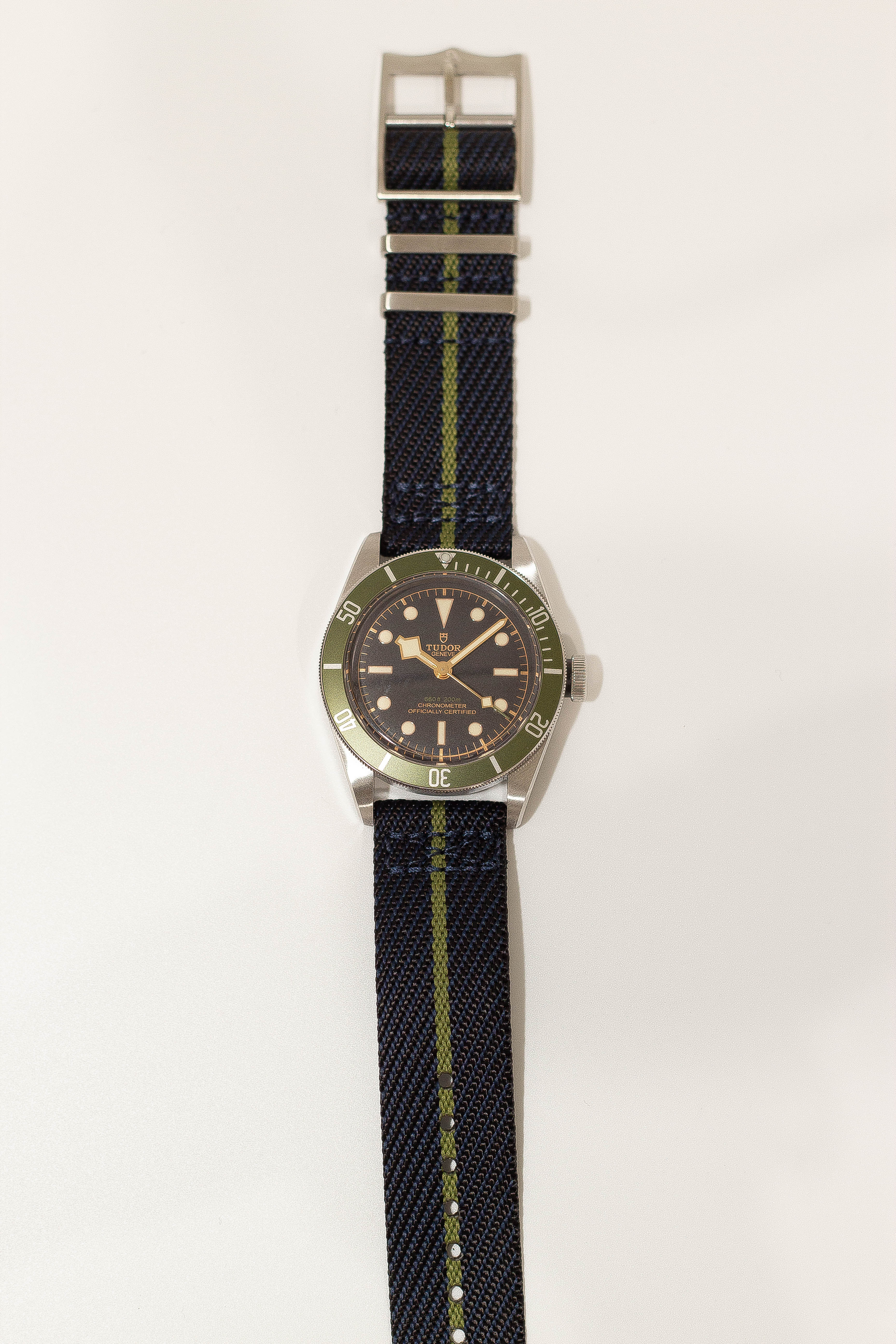 Tudor Black Bay dive watch with green bezel, black dial, and military-style blue-green fabric strap with quick release buckle