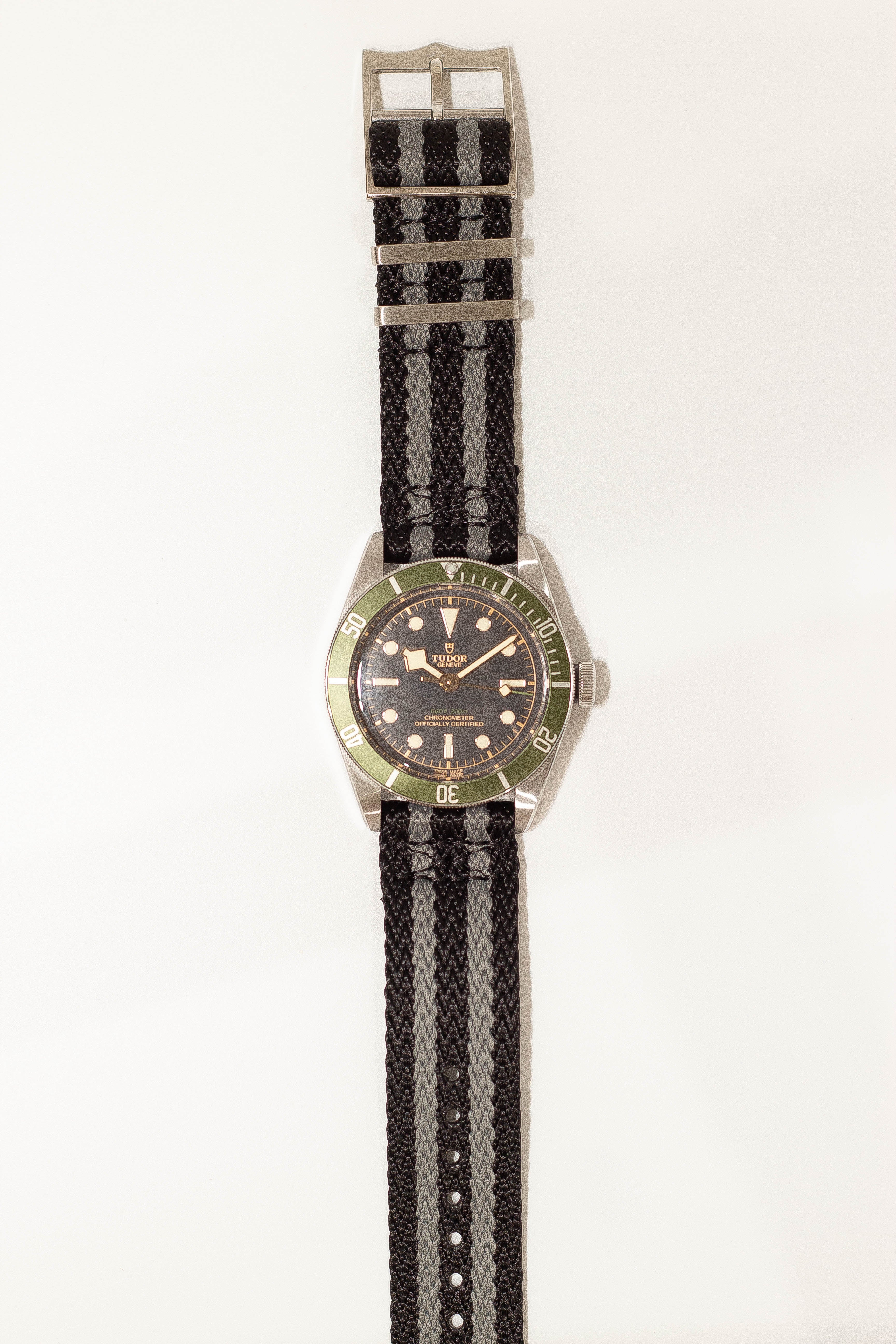 Tudor dive watch with green bezel and black dial on black and grey striped fabric strap with quick release buckle