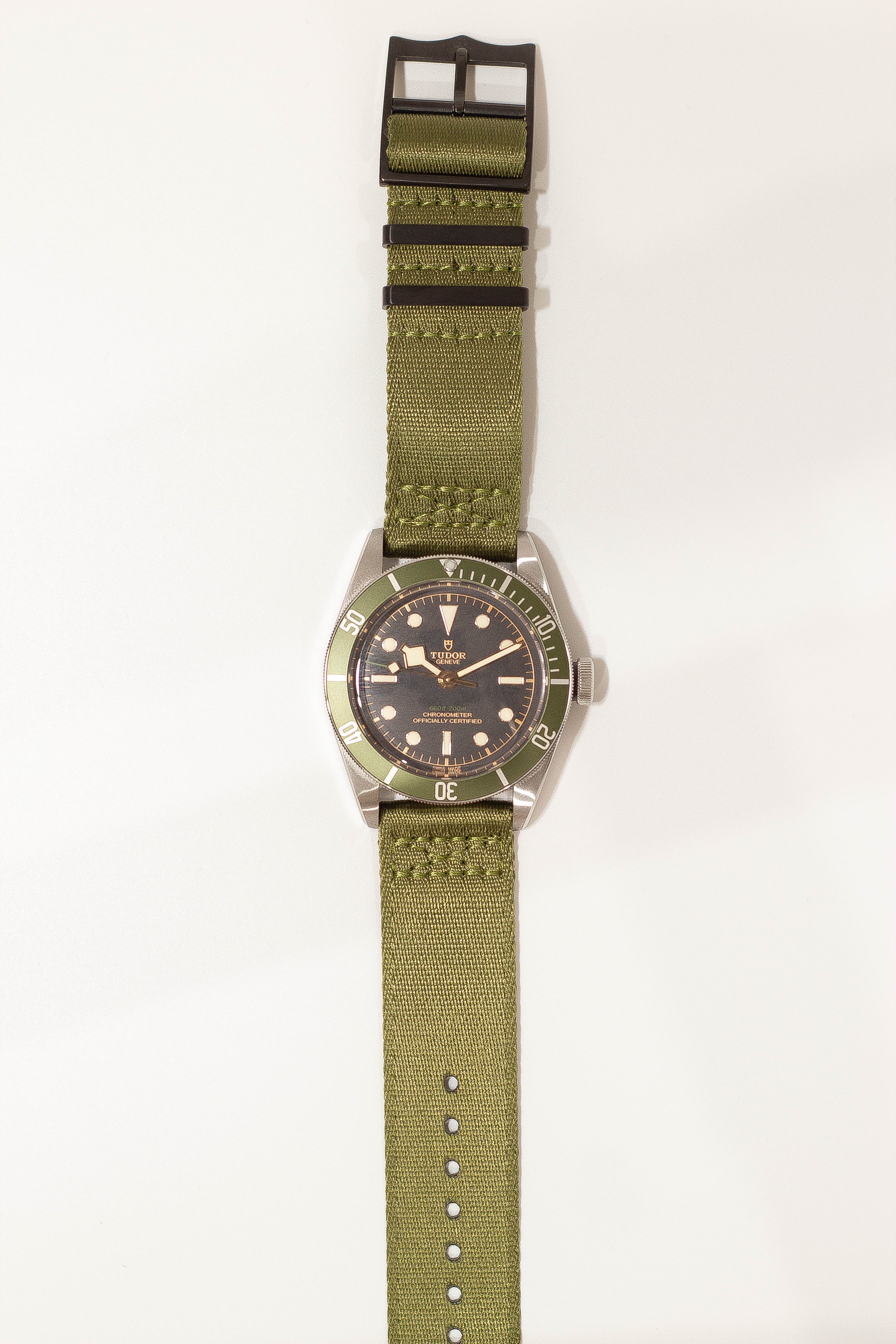 Tudor Black Bay dive watch with green fabric strap and black hardware, featuring dark dial and rotating bezel