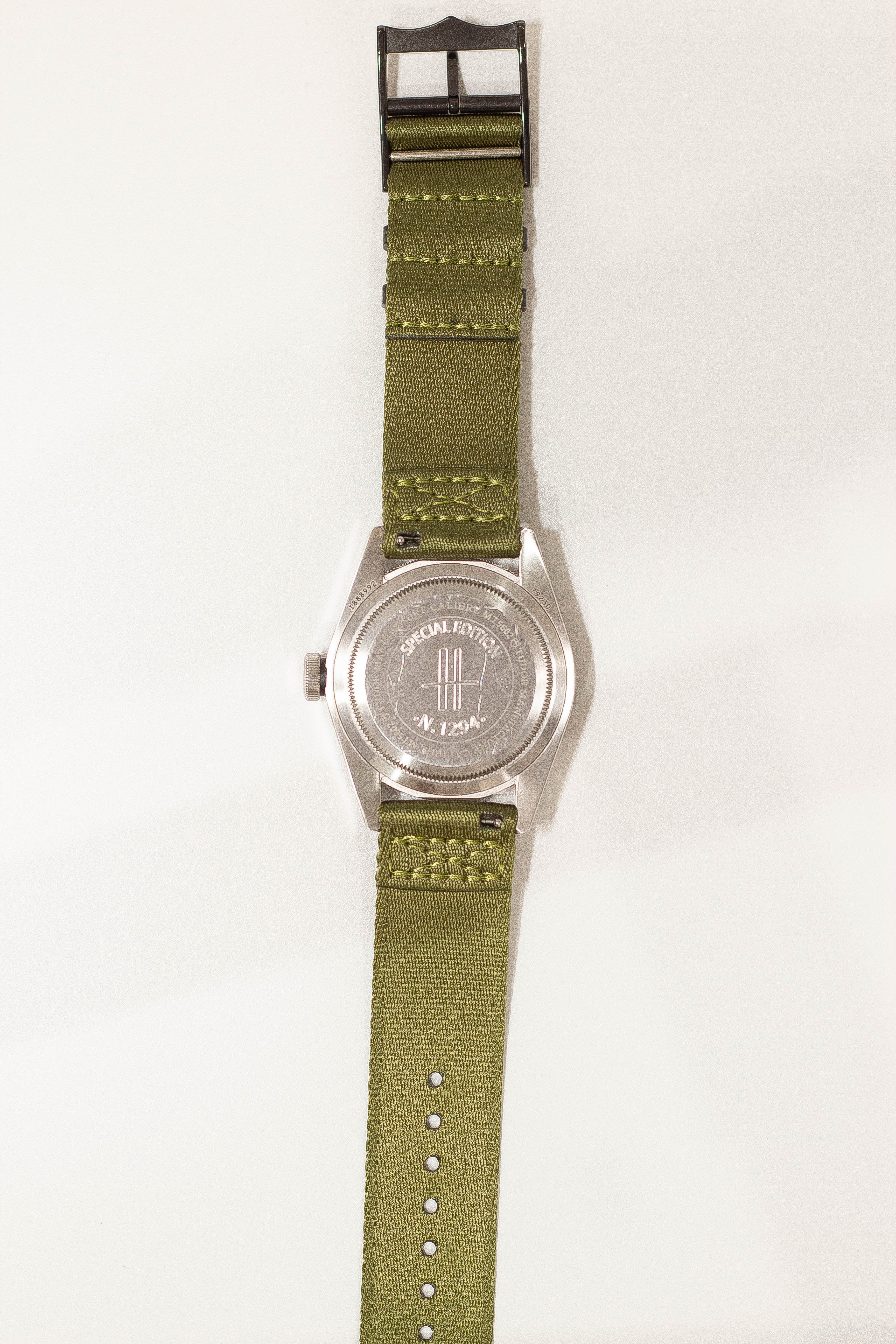 Special edition military watch with stainless steel case, olive green fabric strap, black hardware buckle, and engraved caseback