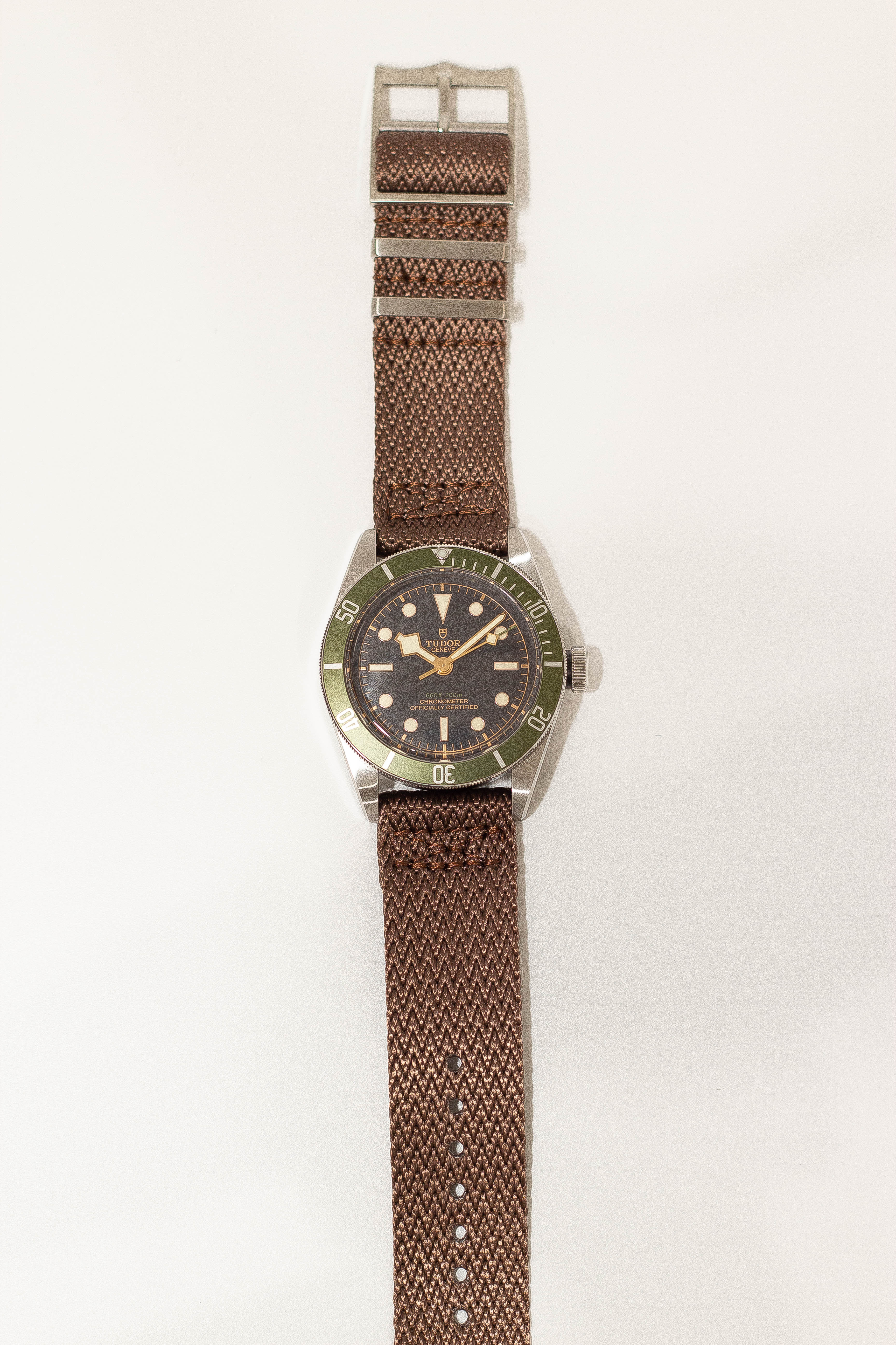 Tudor dive watch with green bezel, black dial, and coffee brown fabric quick release strap with white stitching