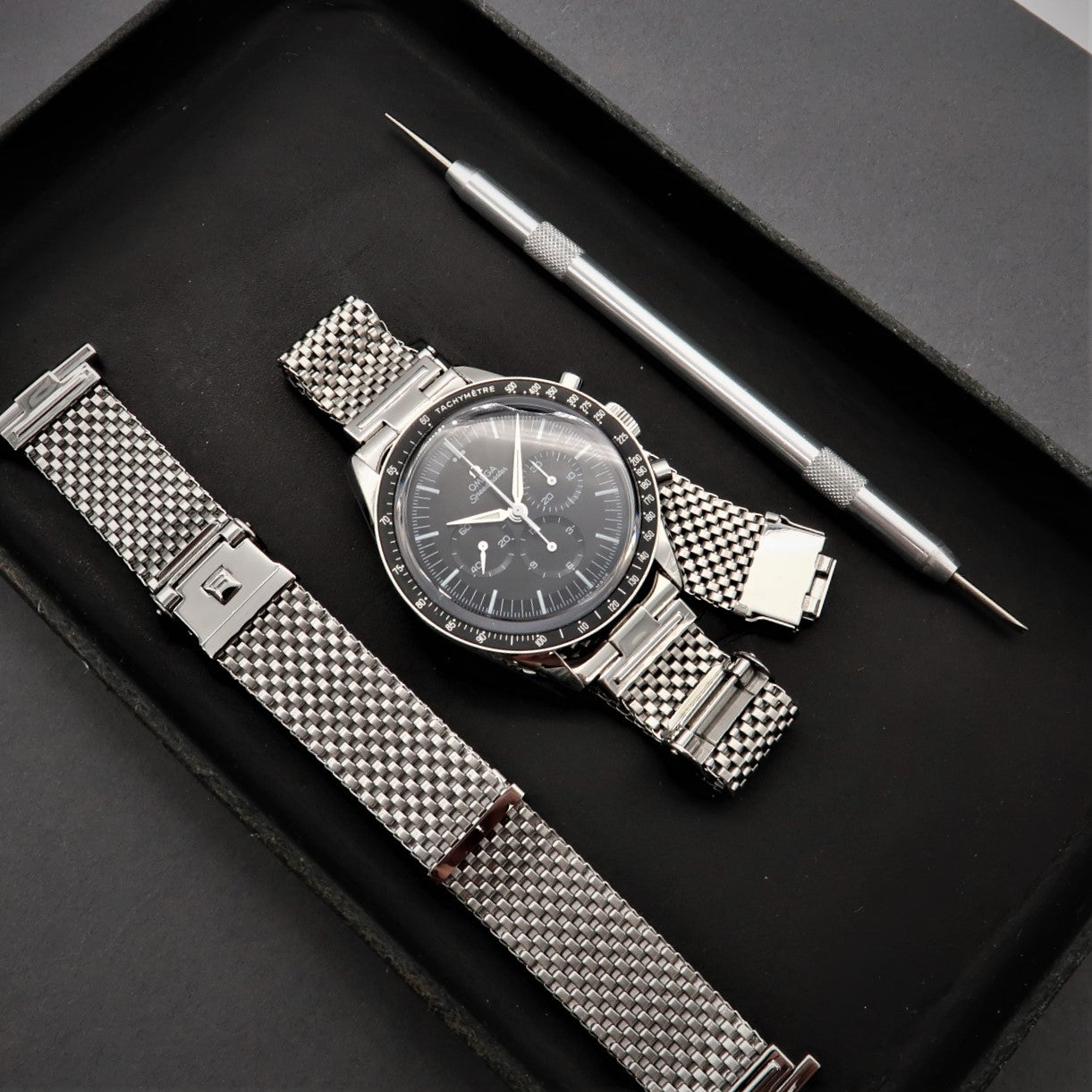Stainless steel mesh watch bracelet with horned ends and adjustment tool on black display tray
