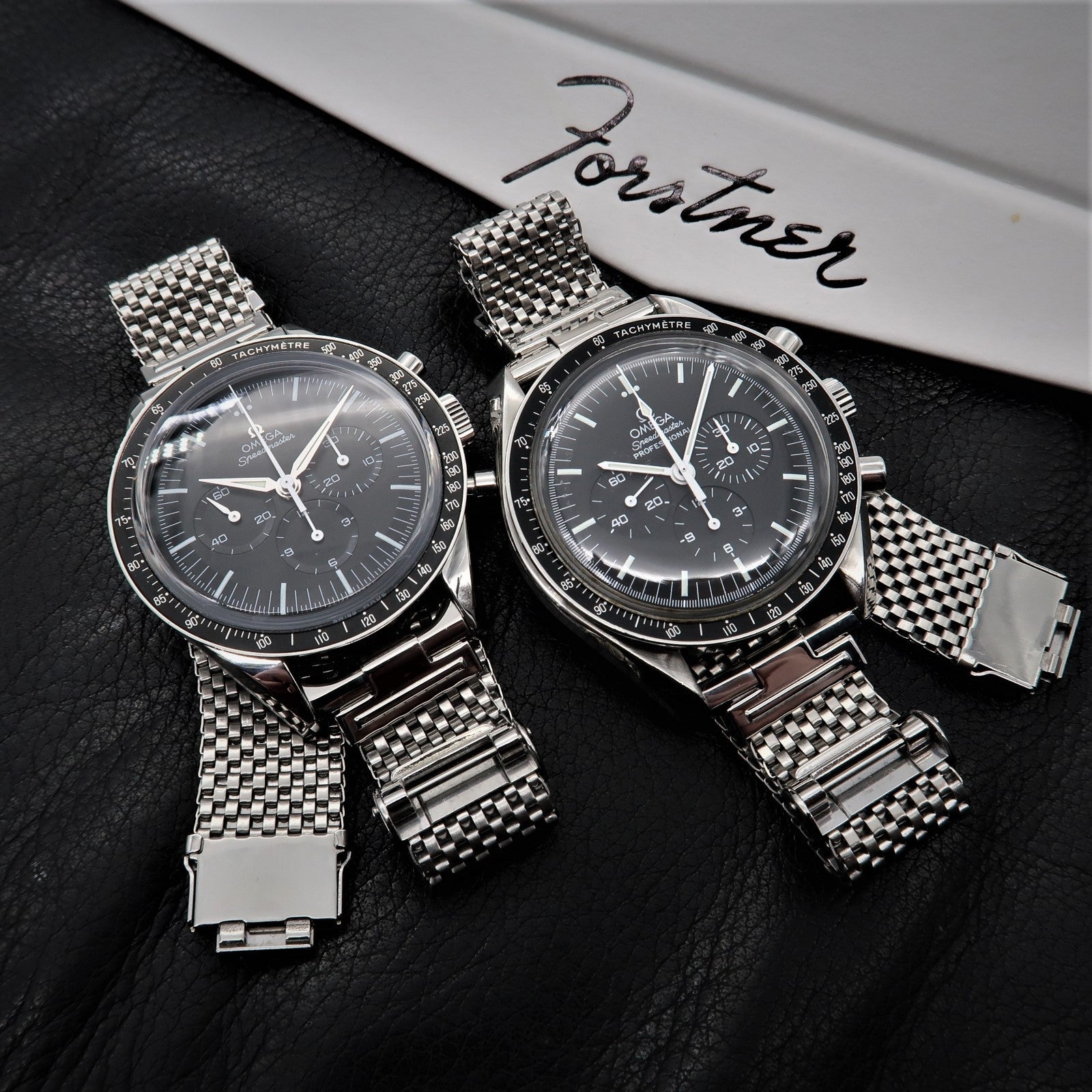 Two stainless steel chronograph watches with mesh bracelets and tachymetre bezels on black leather background