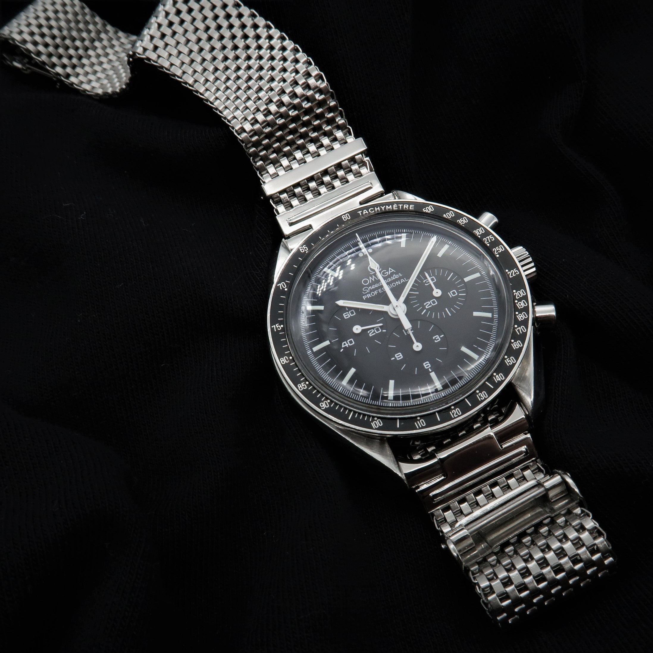 Stainless steel mesh watch bracelet with horned lugs, polished finish and adjustable links on black background