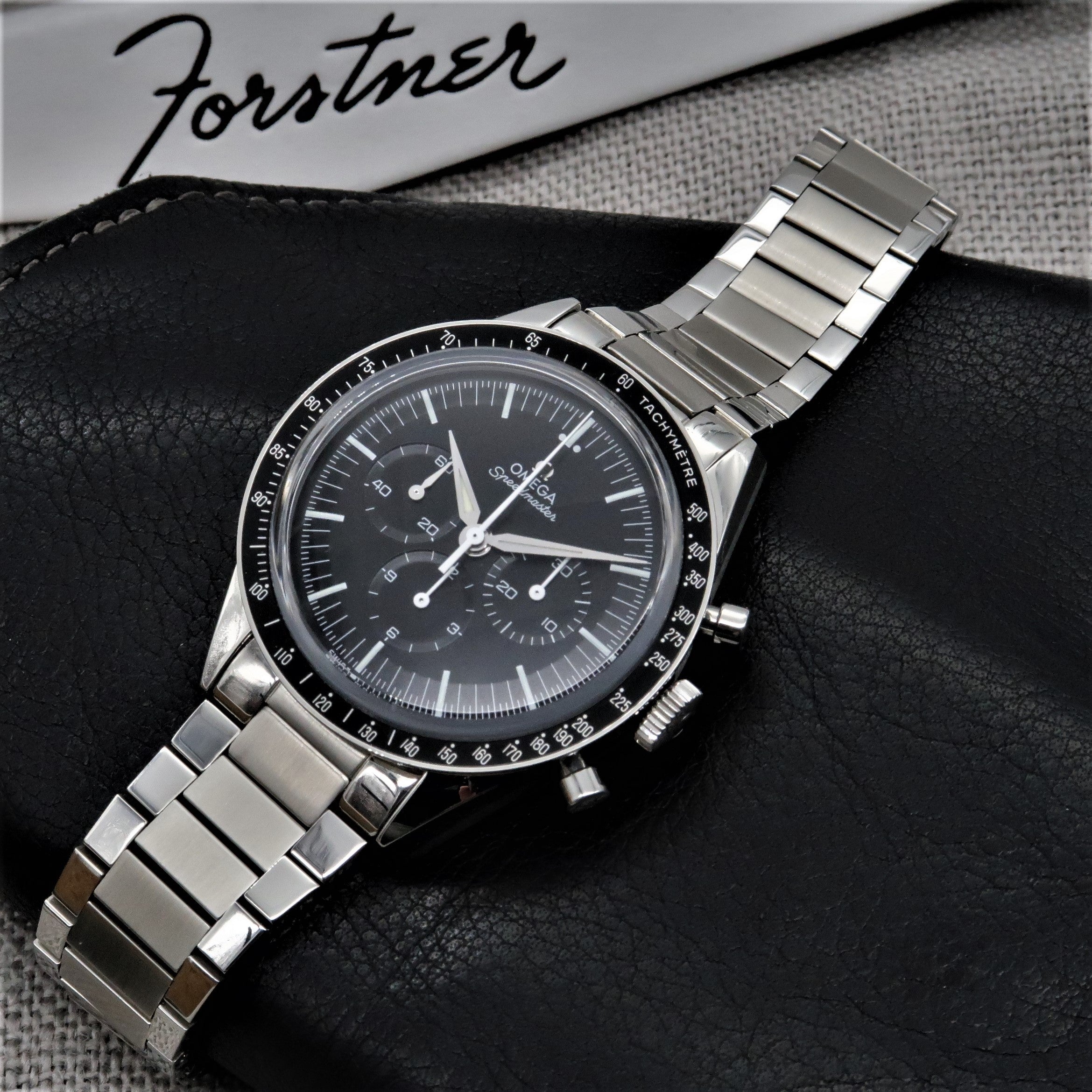 Omega Speedmaster chronograph watch with stainless steel flat link bracelet on black leather, dial detail visible