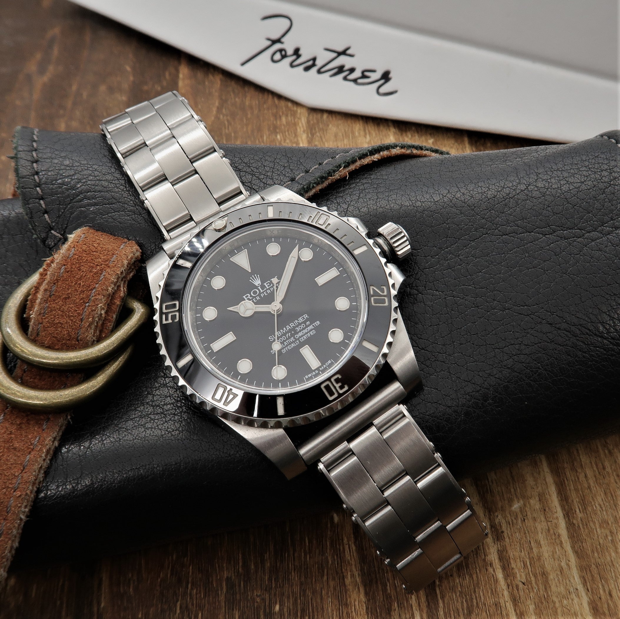 Stainless steel dive watch with black dial and bezel on metal bracelet, displayed on black leather strap