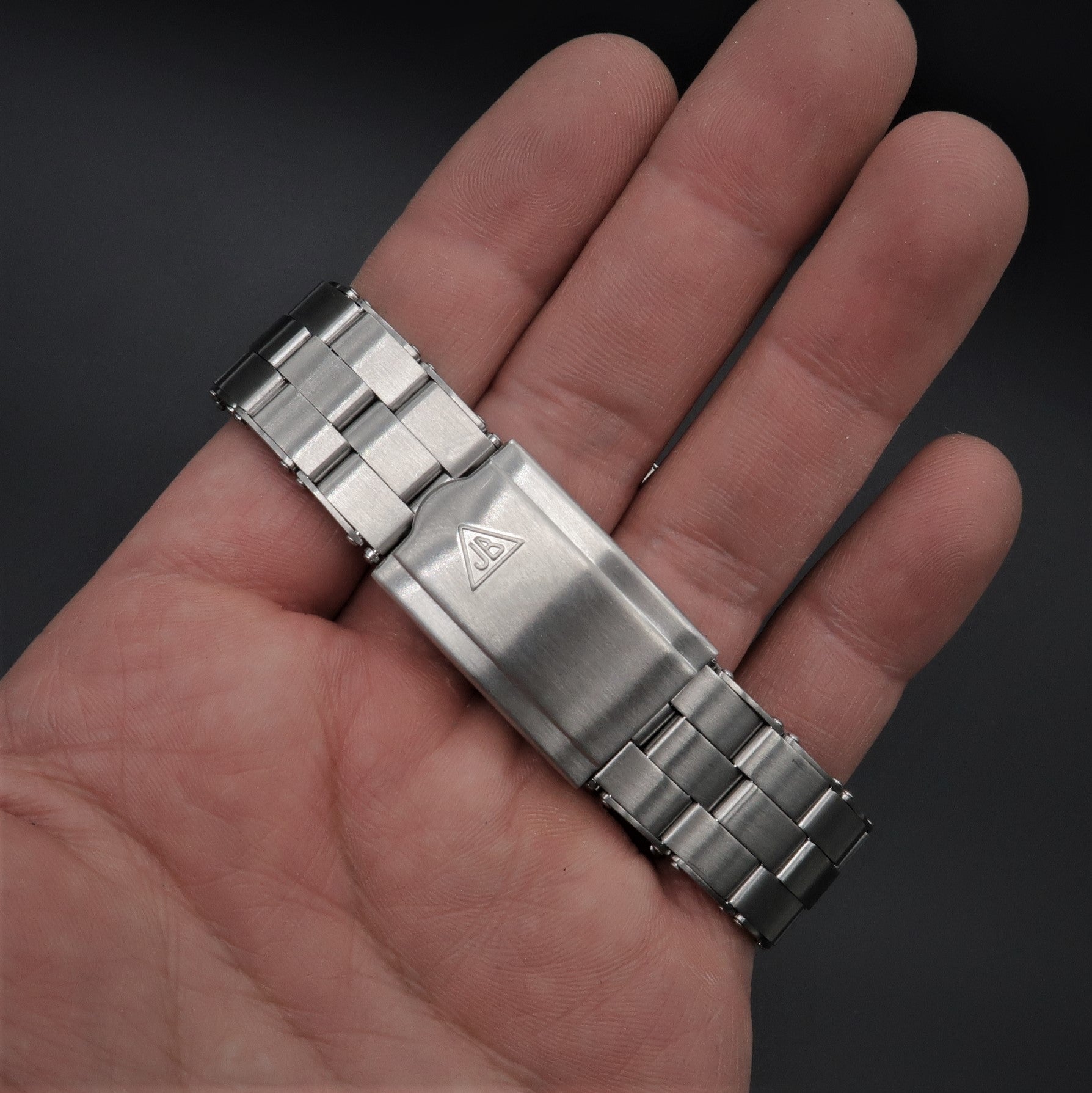 Stainless steel rivet bracelet with solid link segments displayed on palm, showing brushed metal finish and triangle logo detail