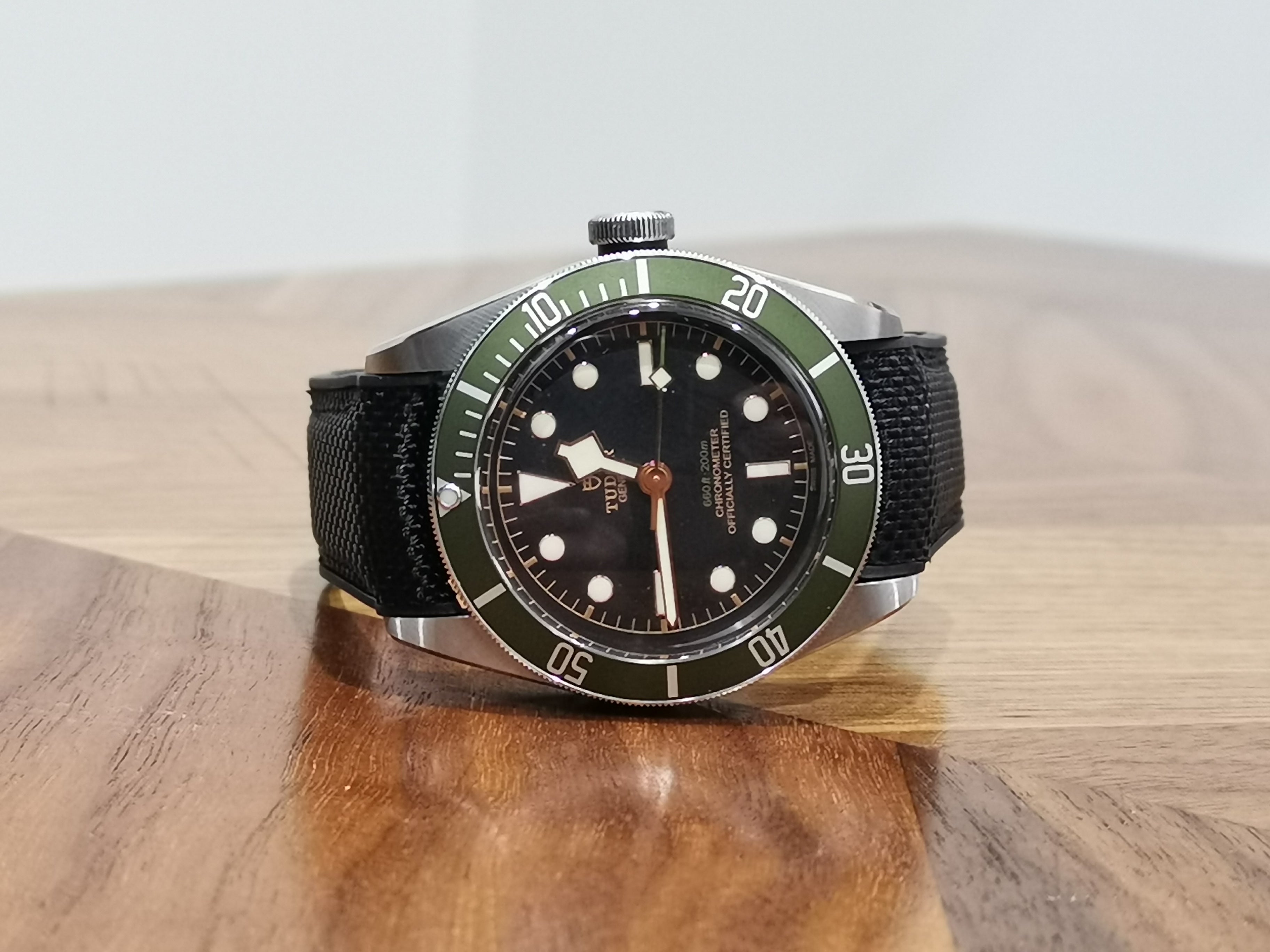 Stainless steel dive watch with green bezel, black dial, and black rubber strap on wooden surface