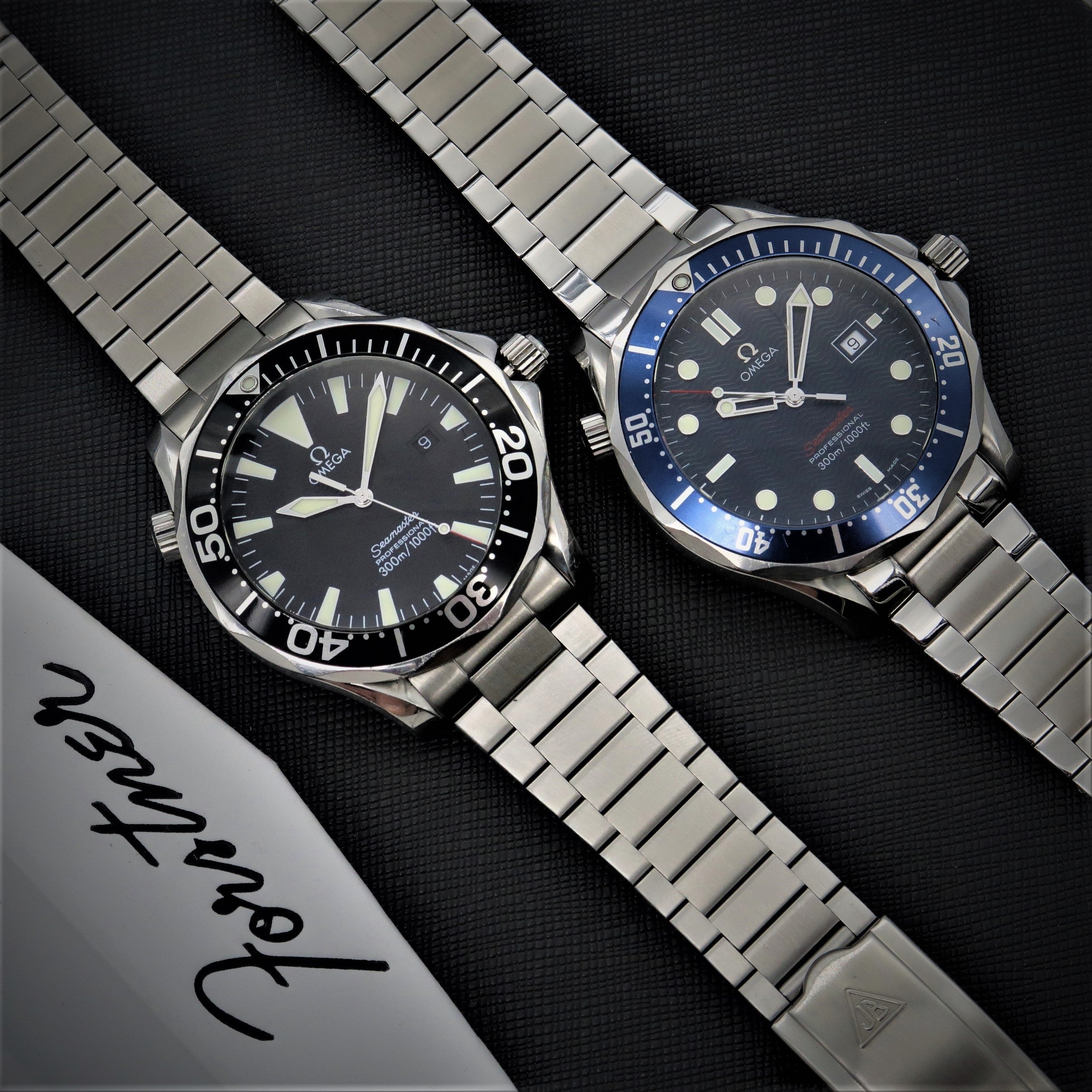 Two Omega Seamaster dive watches with stainless steel Forstner flat link bracelets on black textured background