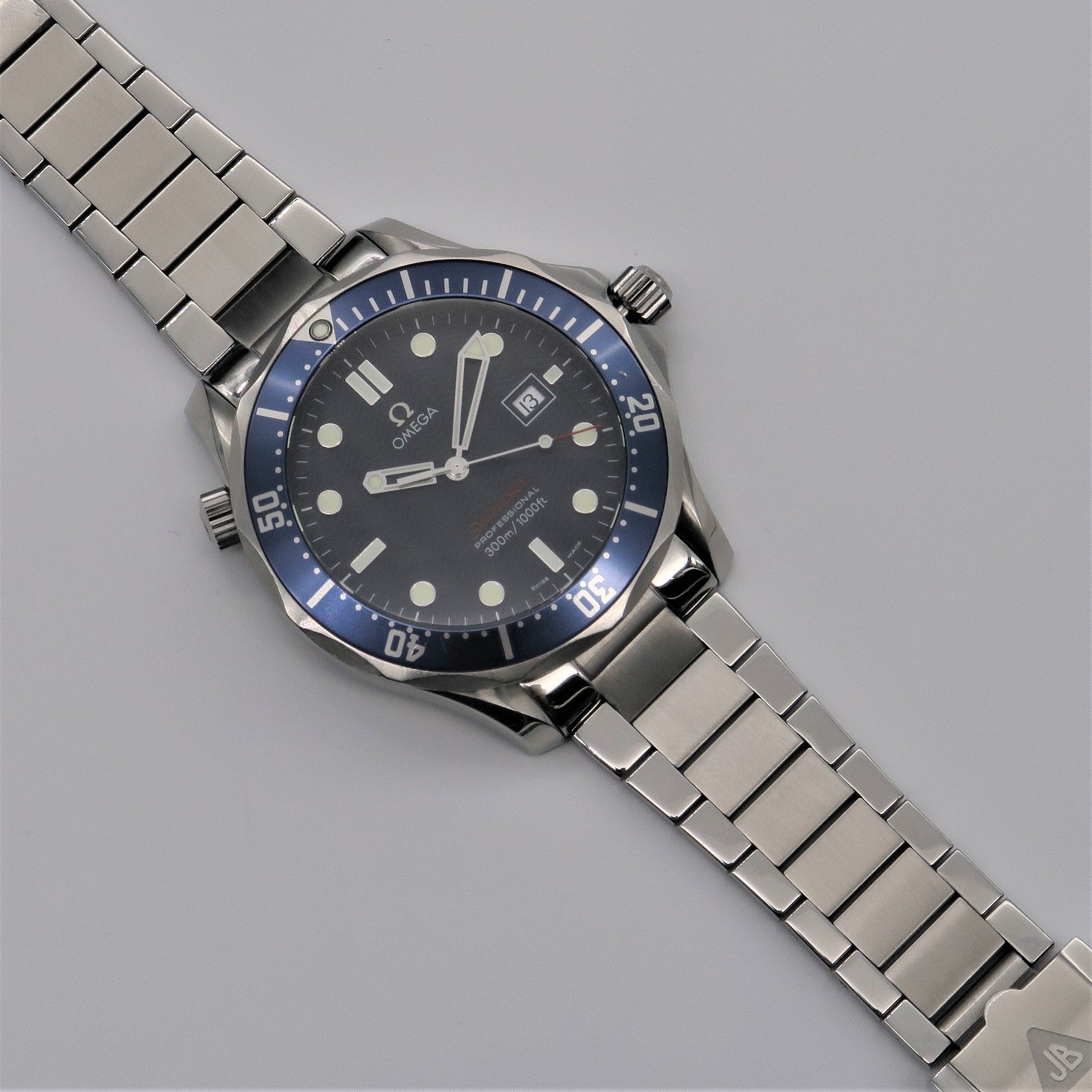 Stainless steel flat link bracelet for Omega Seamaster dive watch with blue bezel and black dial on gray background