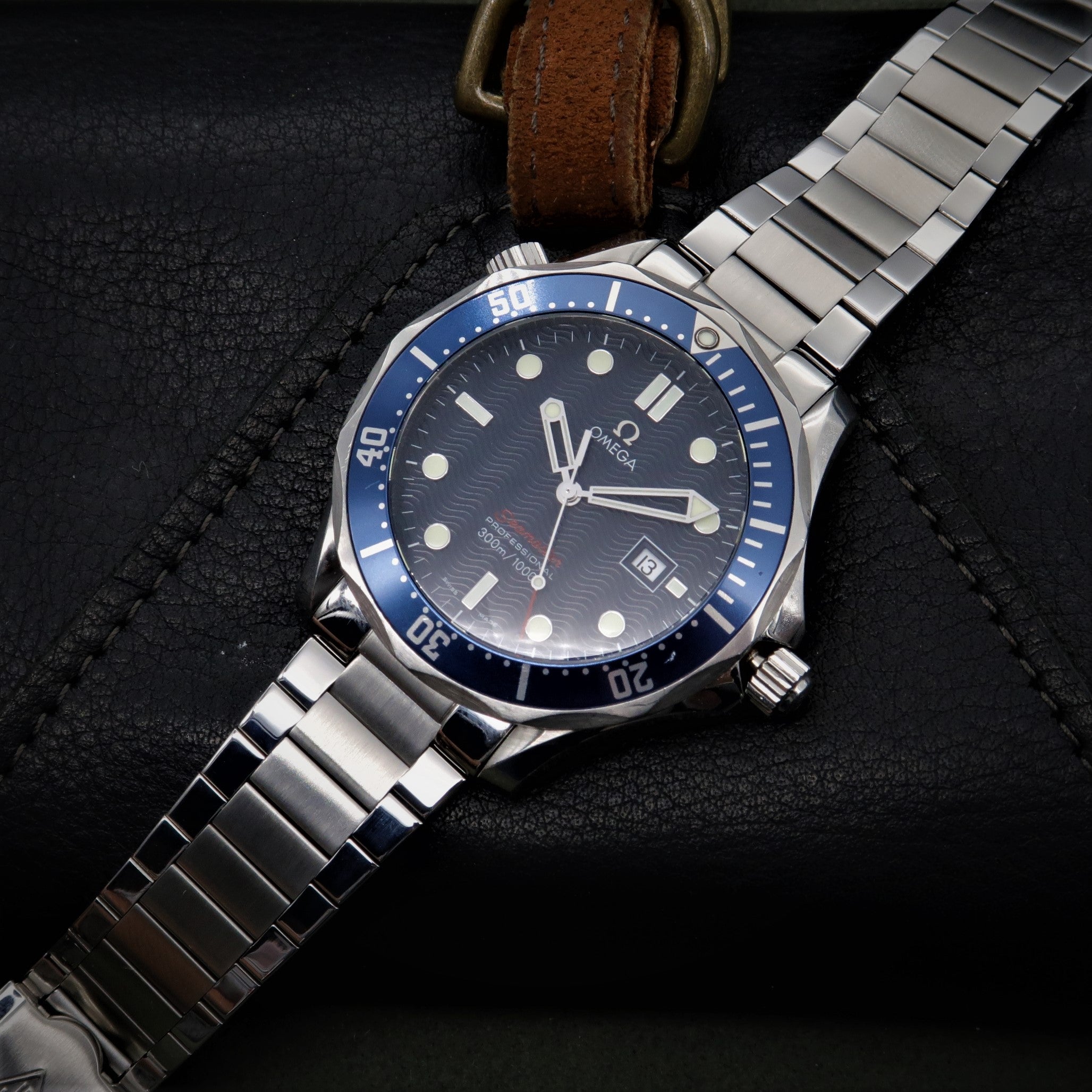 Omega Seamaster dive watch with stainless steel bracelet and blue bezel on dark background with brown leather strap