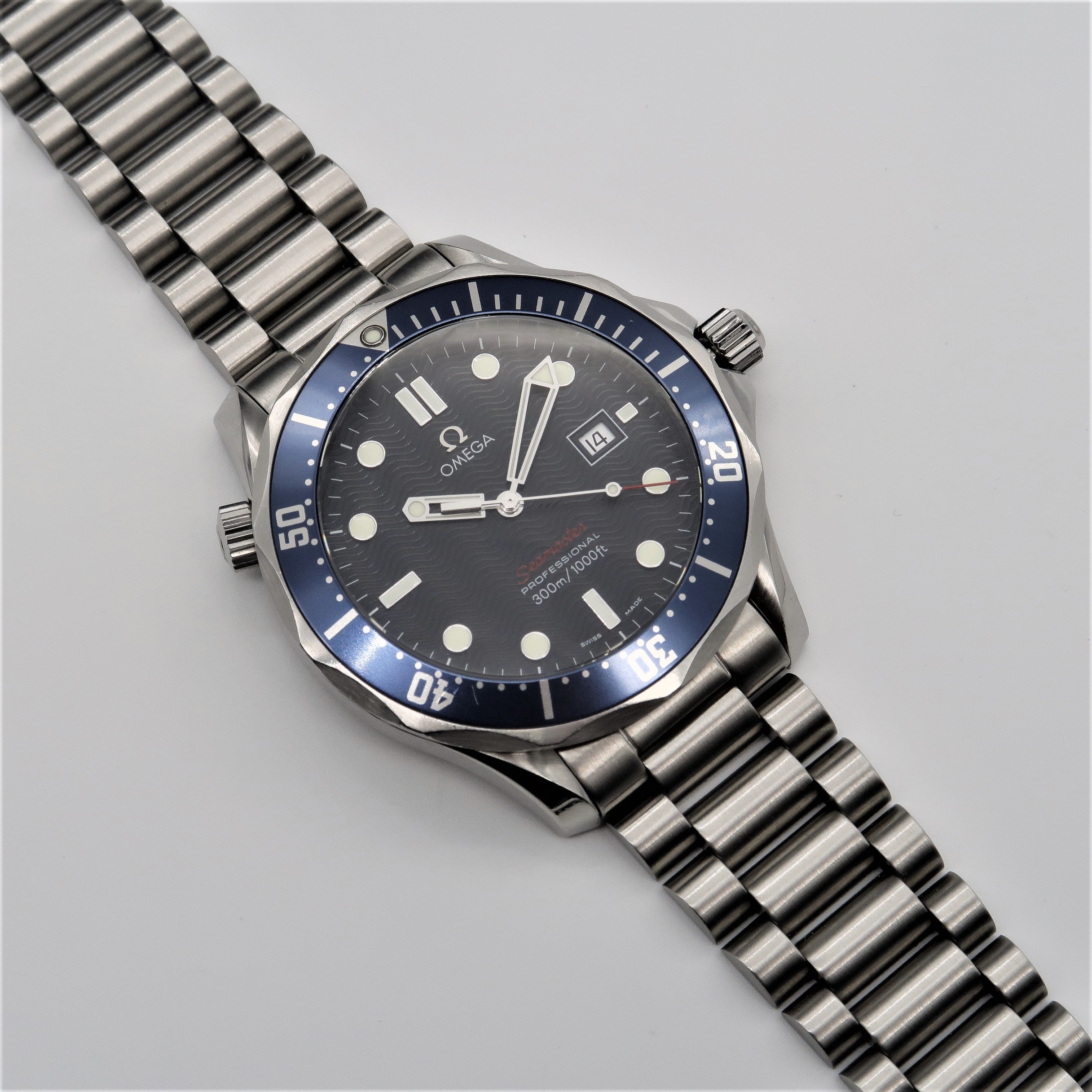 Omega Seamaster dive watch with stainless steel bracelet, blue bezel, black dial, and luminous hands on white background