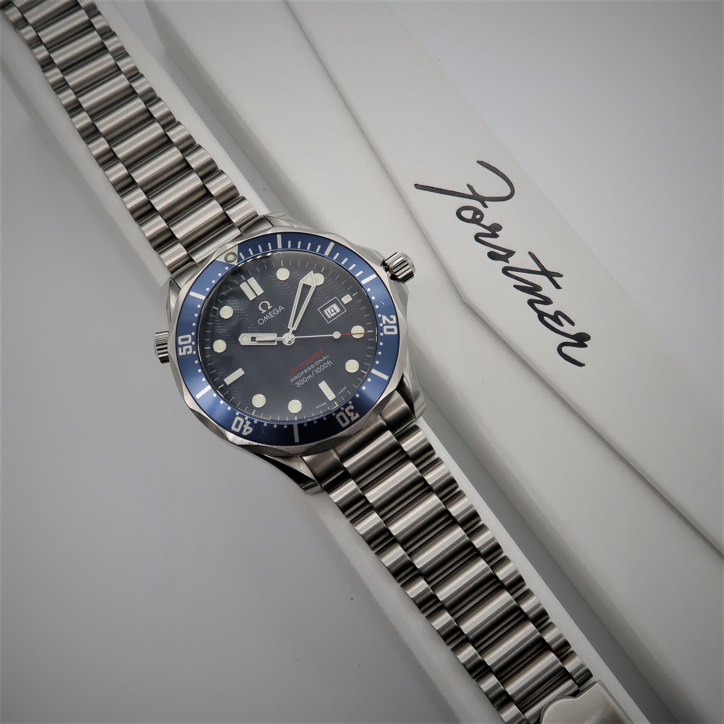 Omega Seamaster automatic dive watch with blue bezel, steel bracelet and black dial on white background