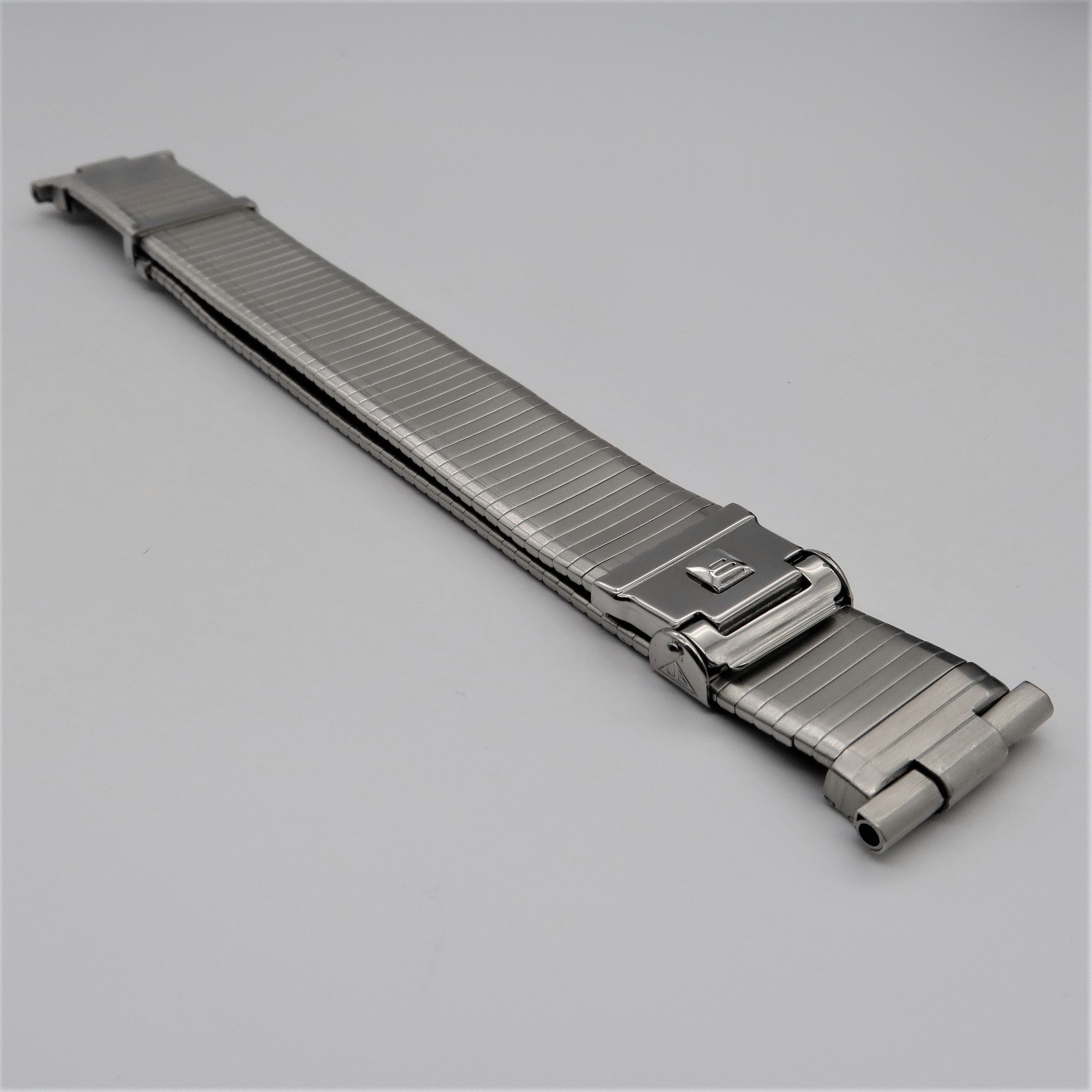 Stainless steel military watch band with thin profile and fold-over deployment clasp on gray background