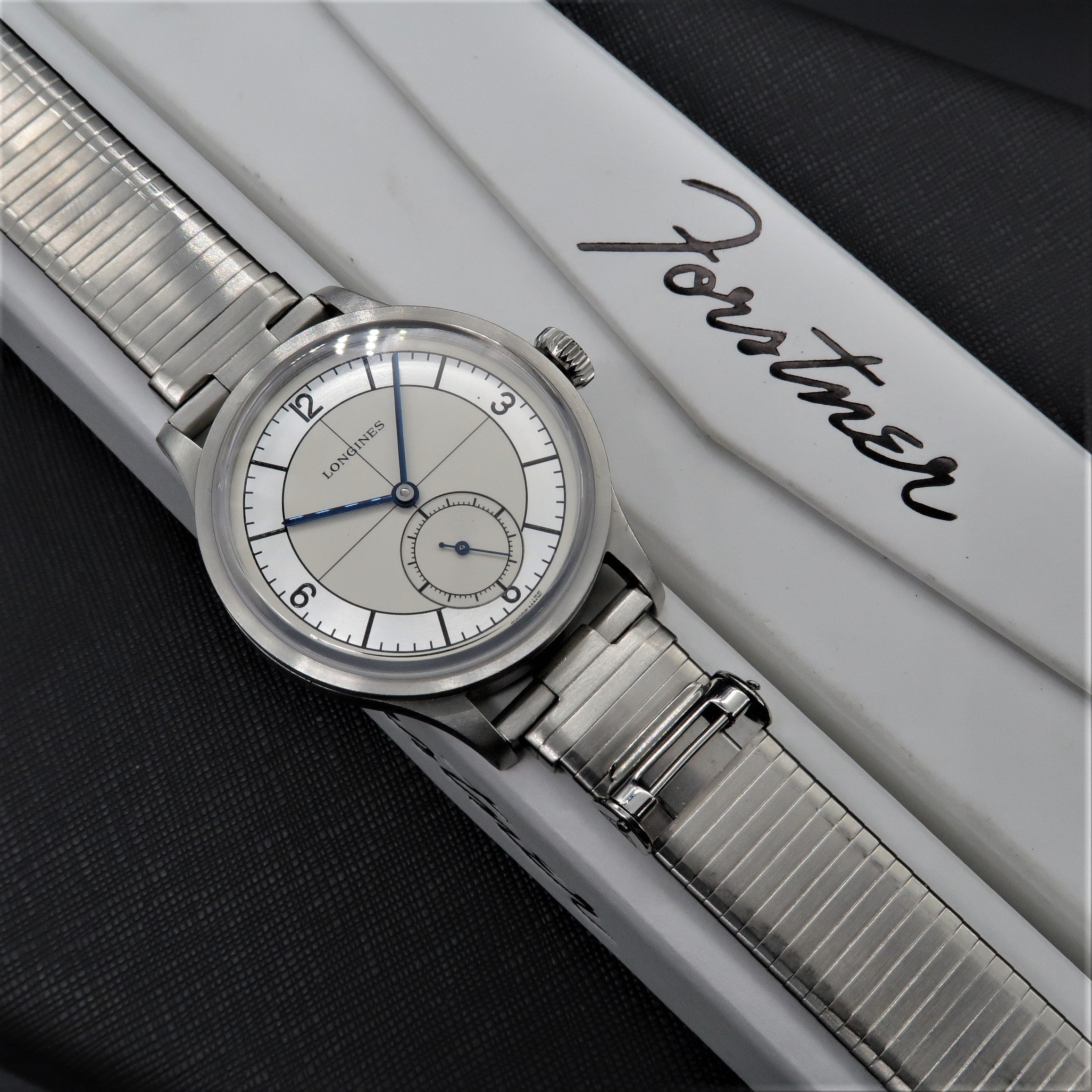 Longines Heritage stainless steel watch with silver dial, blue hands, and metal bracelet on white branded presentation box