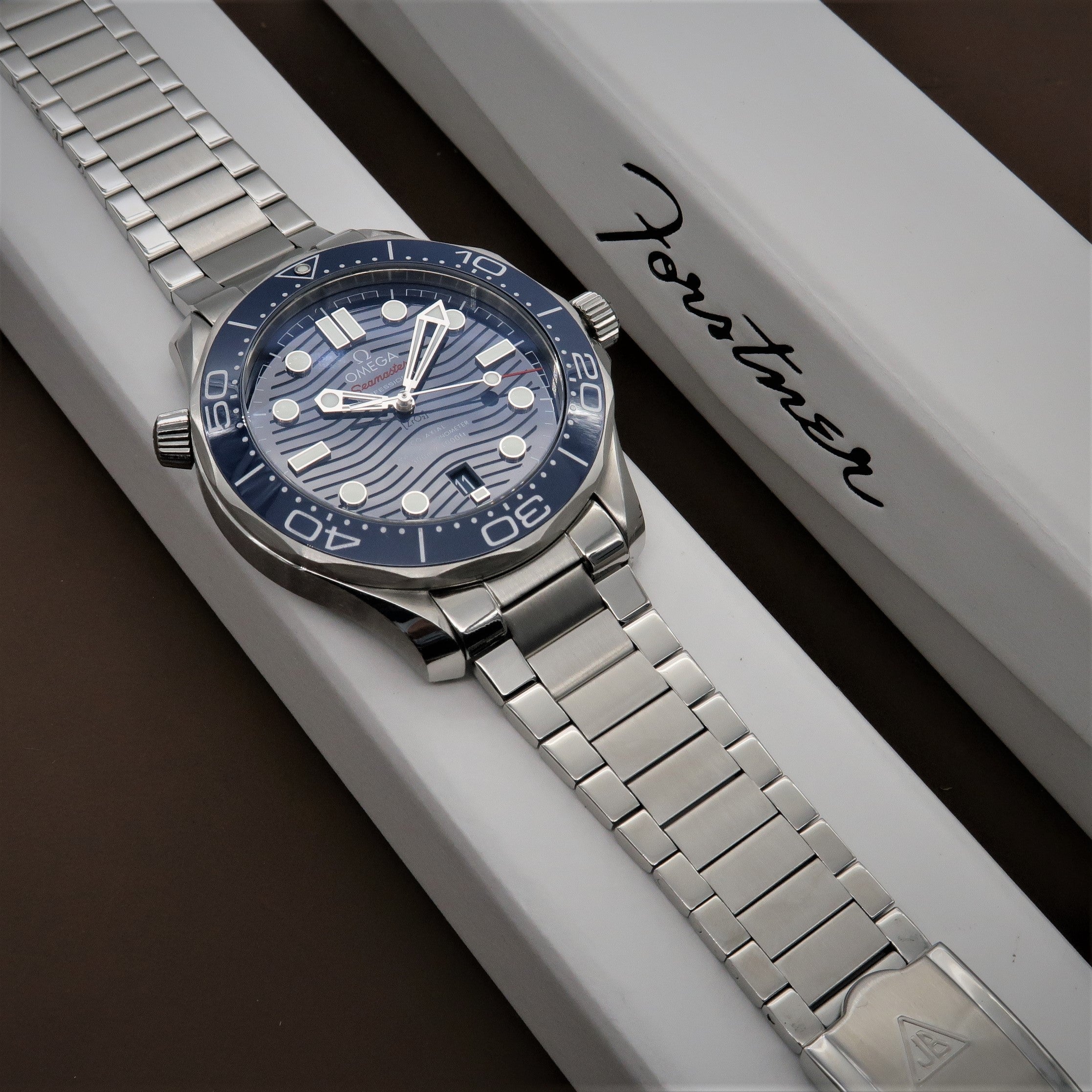 Stainless steel dive watch with blue dial and wave pattern on white presentation box with bracelet